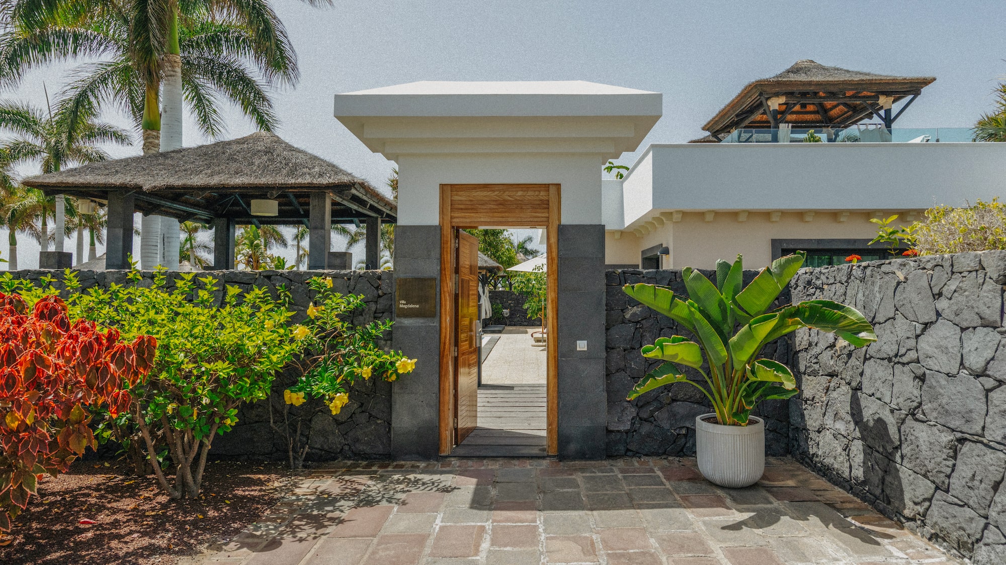 Villa Magdalena entrance gate with tropical garden, stone wall, and palm trees.