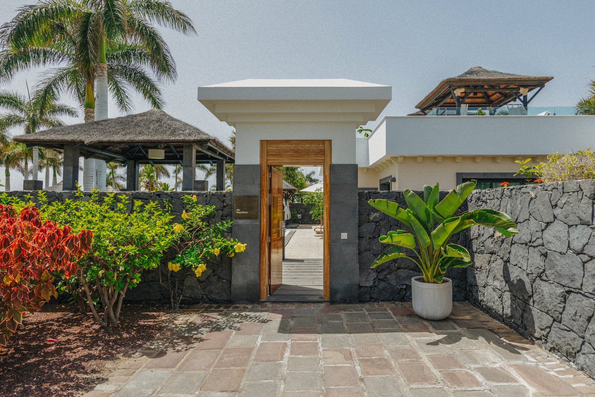 Villa Magdalena entrance gate with tropical garden, stone wall, and palm trees.