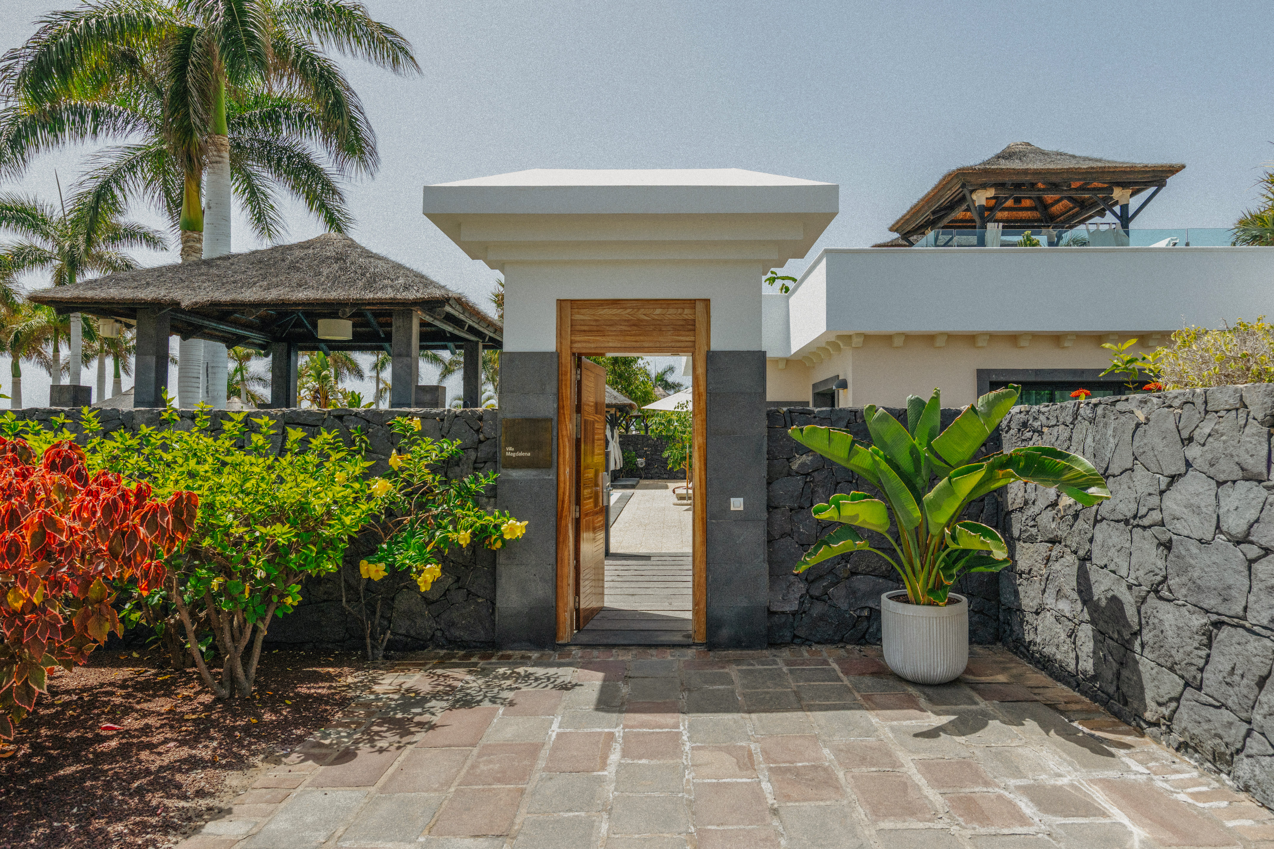 Villa Magdalena entrance gate with tropical garden, stone wall, and palm trees.