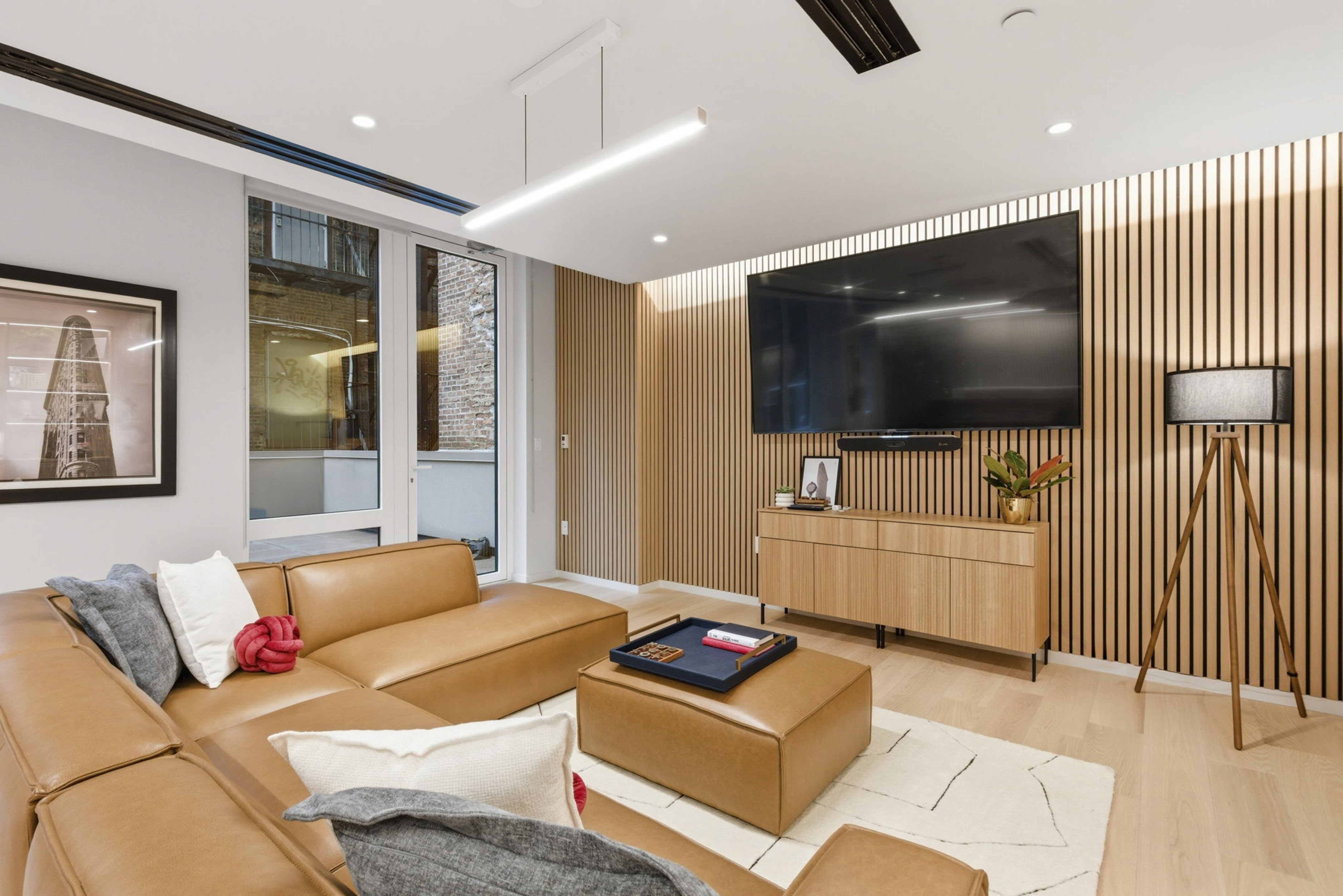 Modern living room with brown leather sectional, wood slat accent wall, large TV.