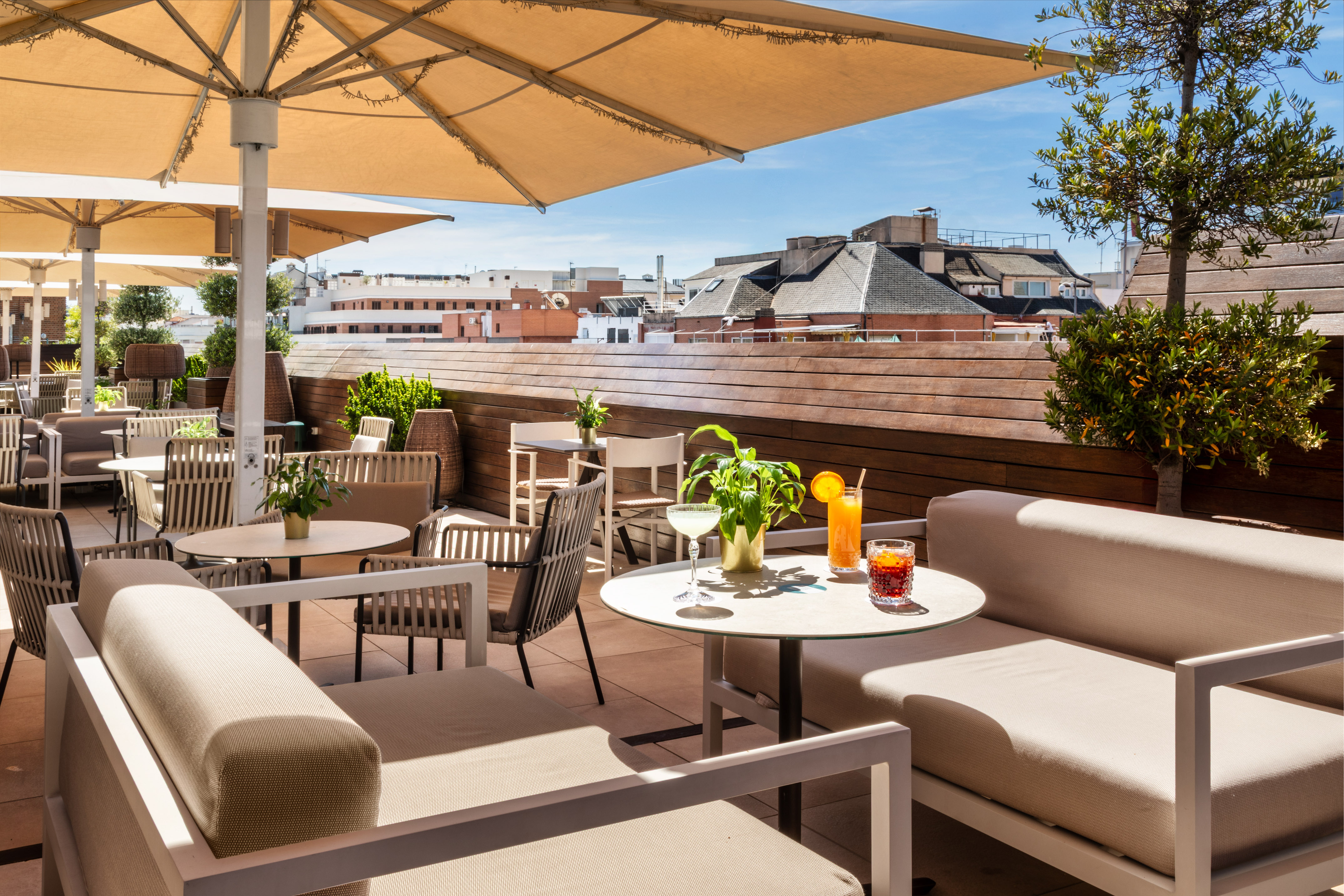 Sunny rooftop terrace with modern outdoor seating, umbrellas, cocktails, and city view.