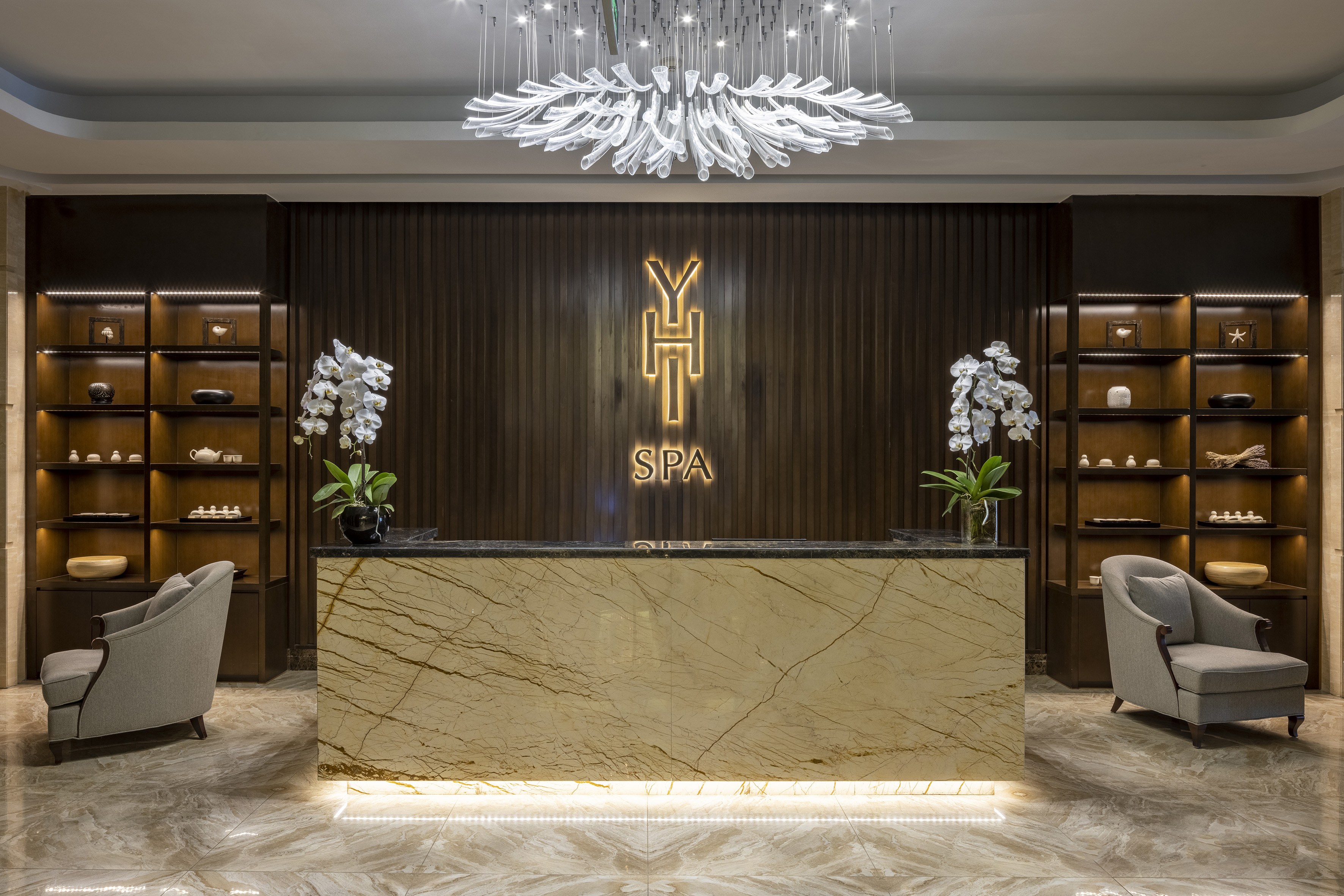 Luxury YHT Spa reception with marble desk, modern chandelier, orchids, and shelves.