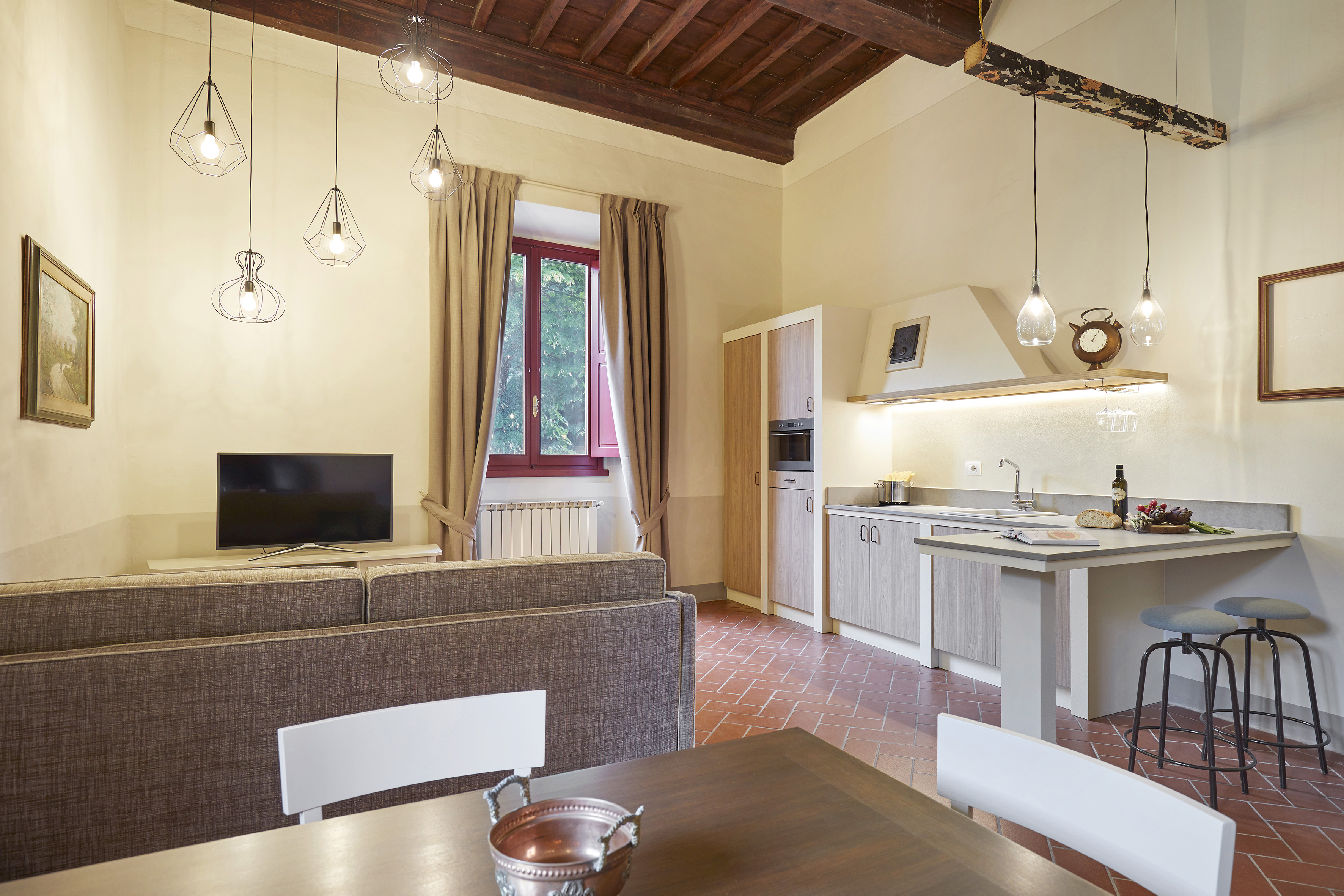 Open-plan living area and modern kitchen with terracotta floor, exposed beams.