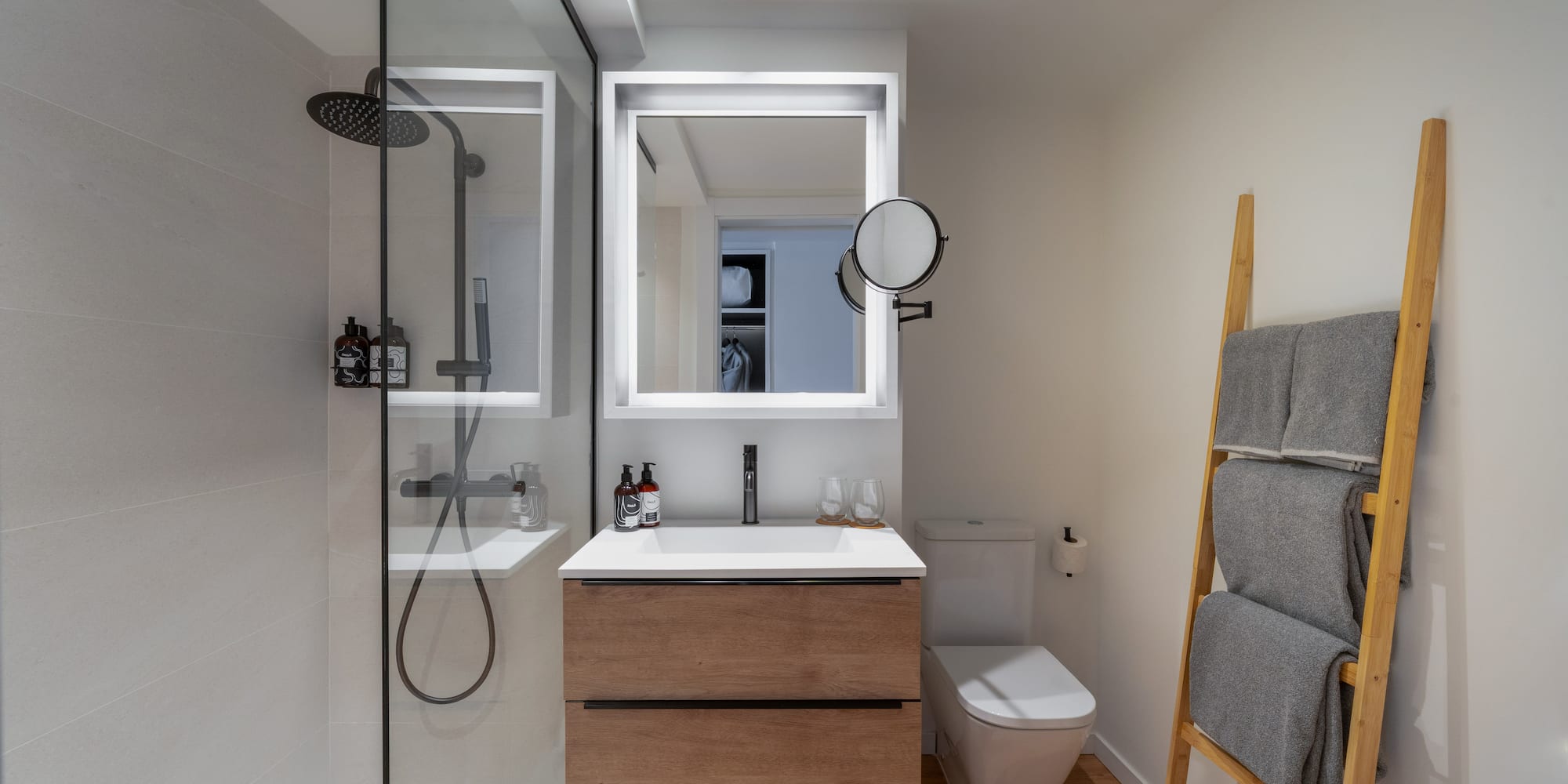 Diseño de baño moderno con ducha de cristal, mueble de madera y espejo LED.