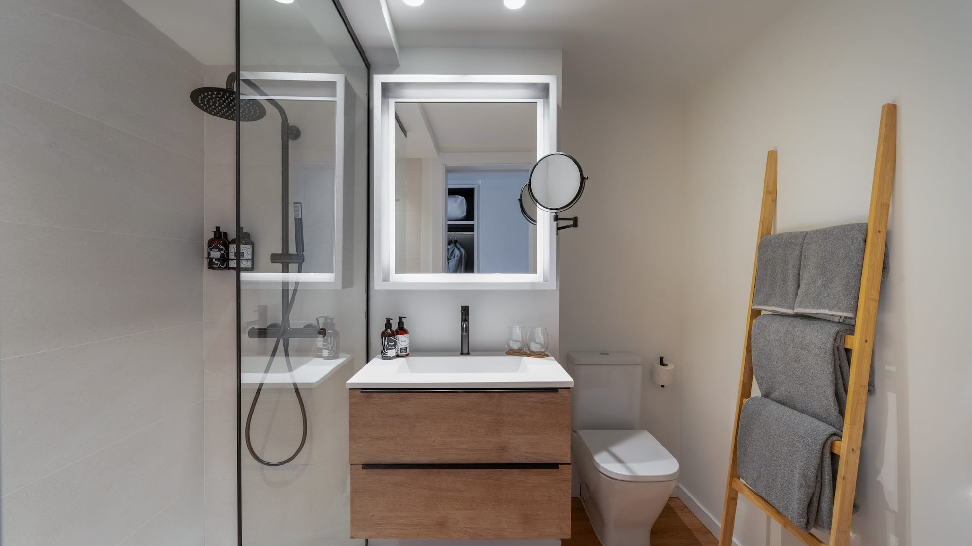 Diseño de baño moderno con ducha de cristal, mueble de madera y espejo LED.