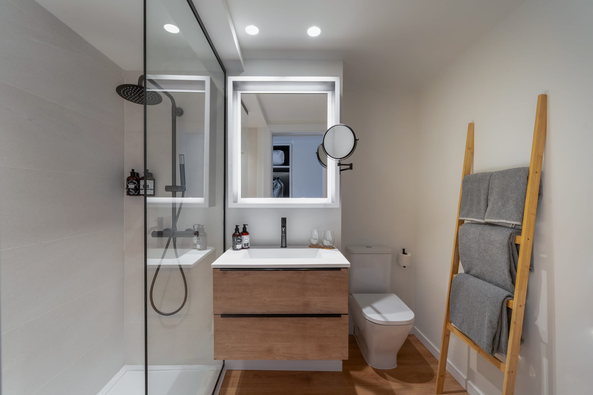 Diseño de baño moderno con ducha de cristal, mueble de madera y espejo LED.