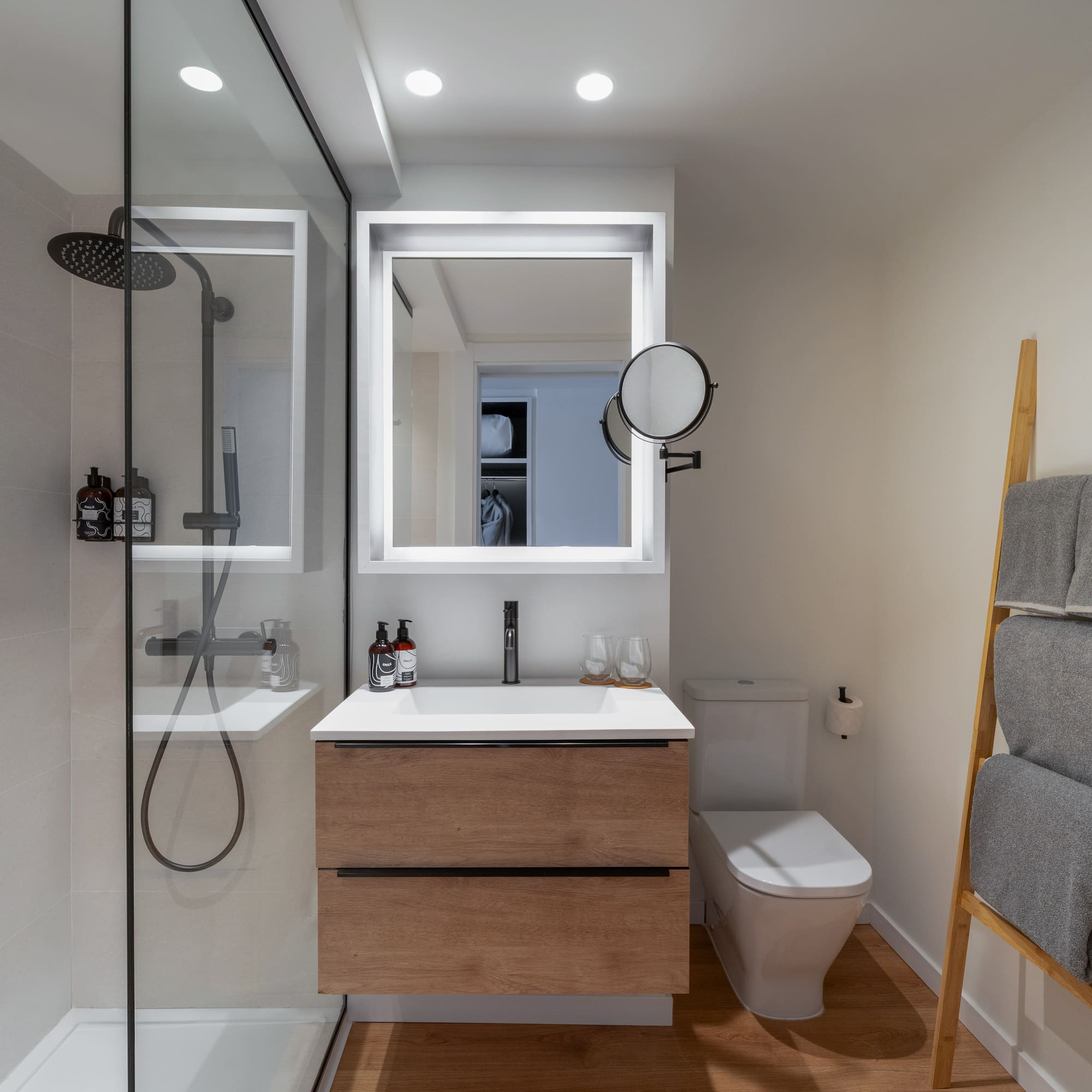 Diseño de baño moderno con ducha de cristal, mueble de madera y espejo LED.