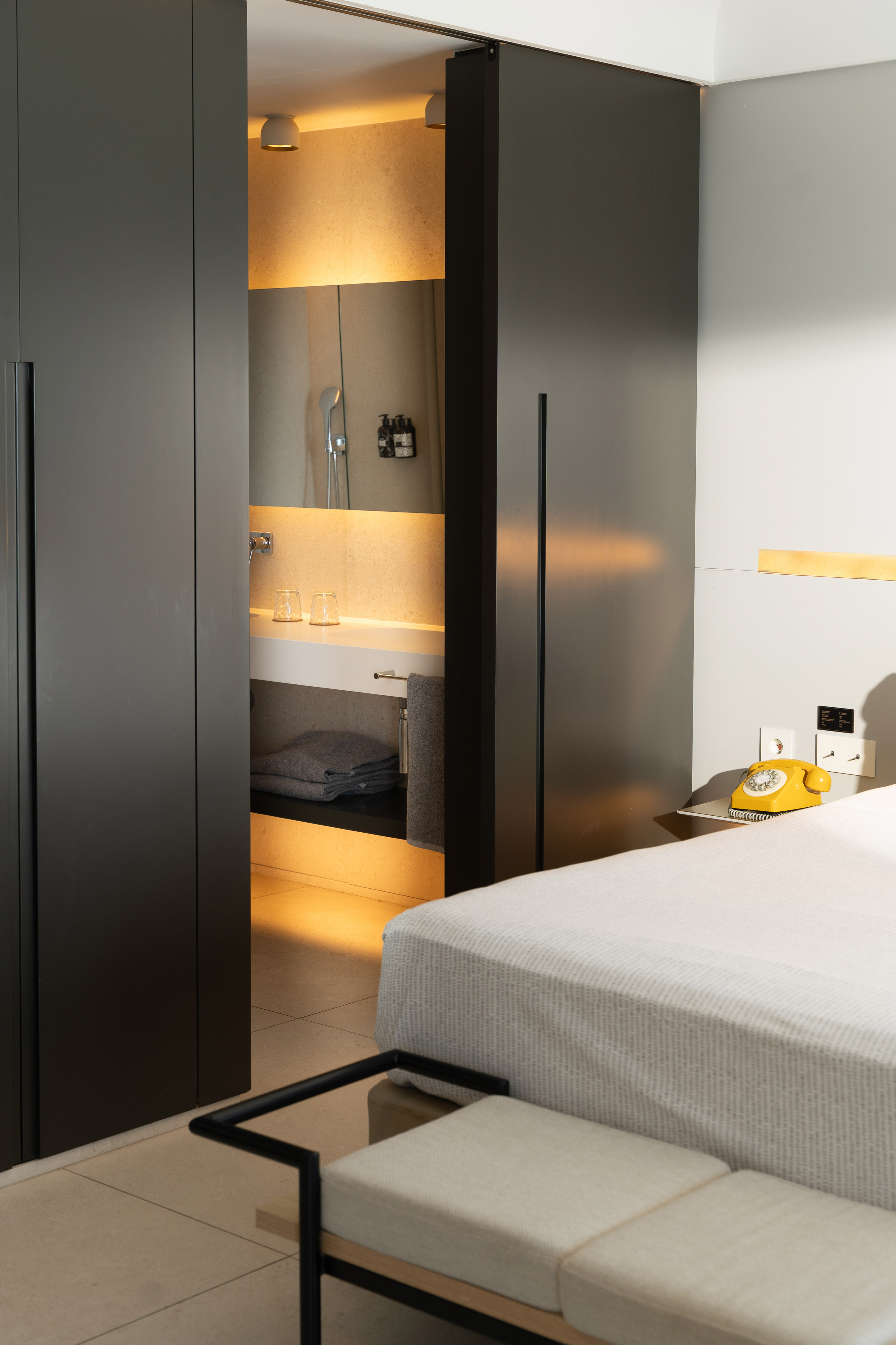 Modern bedroom with open sliding door to lit bathroom, retro yellow phone.