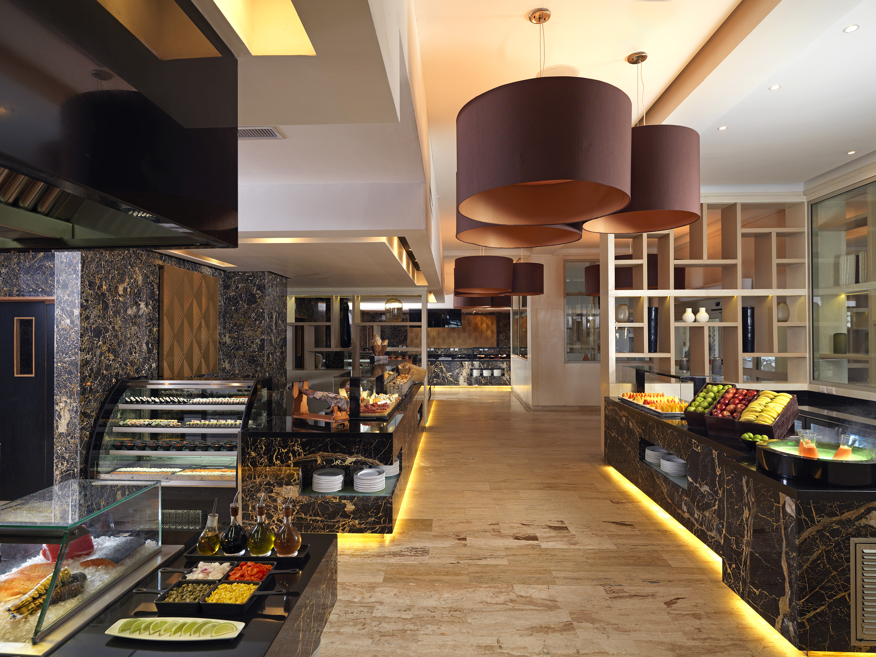 Upscale buffet restaurant with marble counters, sushi bar, fresh fruit, and pendant lights.