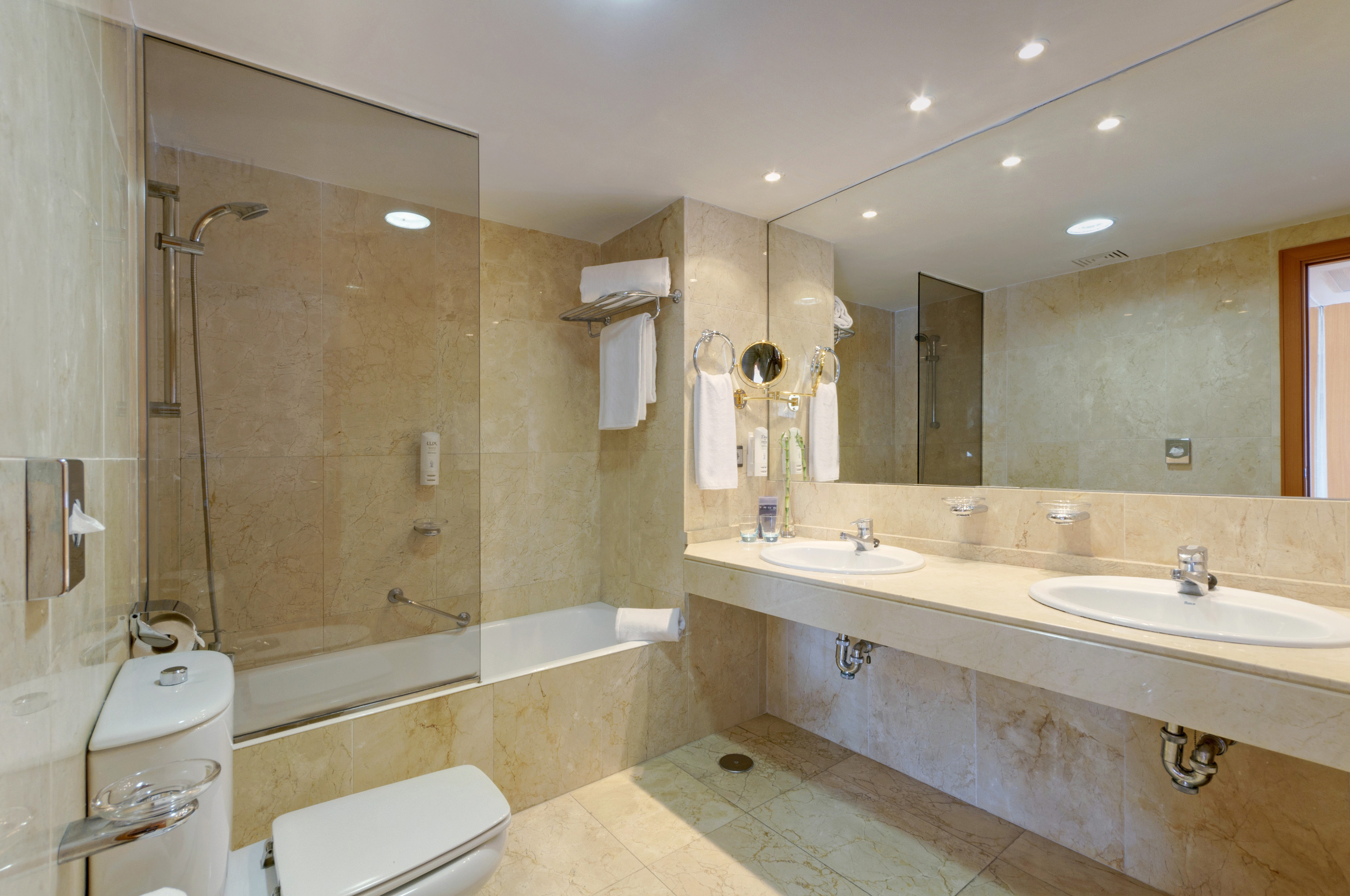 Elegant beige marble bathroom with bathtub, glass shower, double sinks, and mirror.