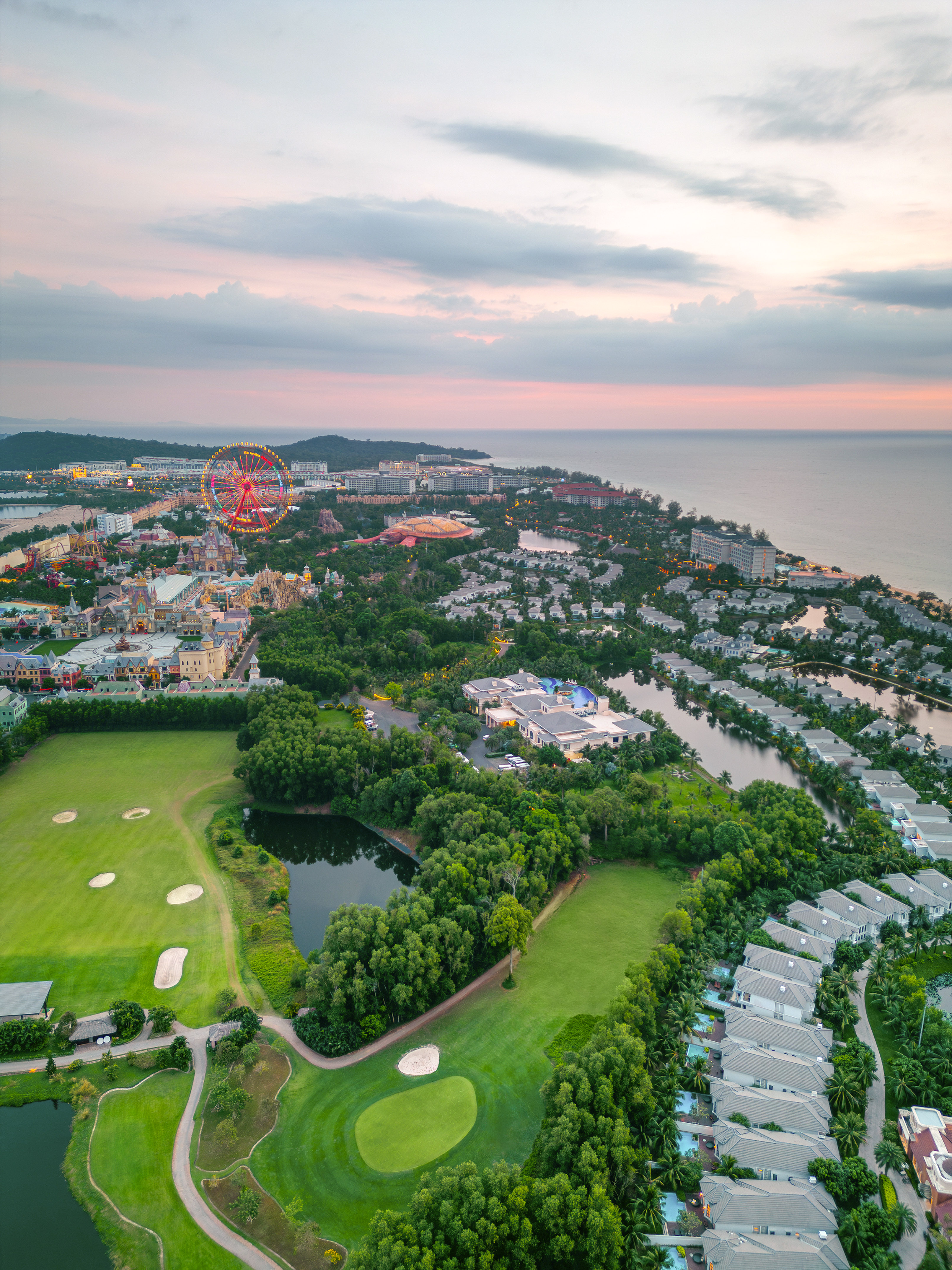 Phu Quoc coastal resort with golf course, theme park, and ocean at sunset.
