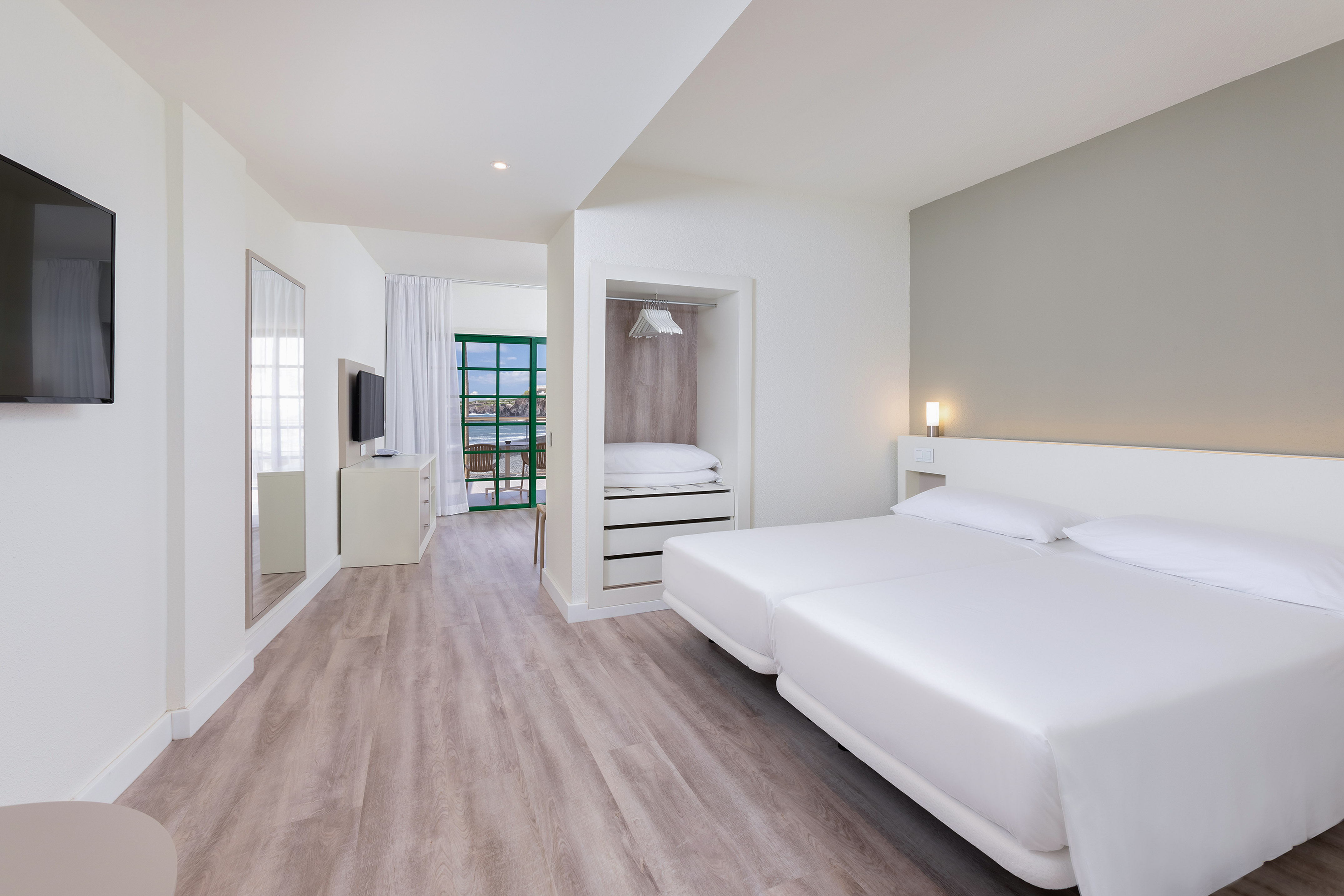 Modern hotel room with twin beds, balcony ocean view, and built-in wardrobe.