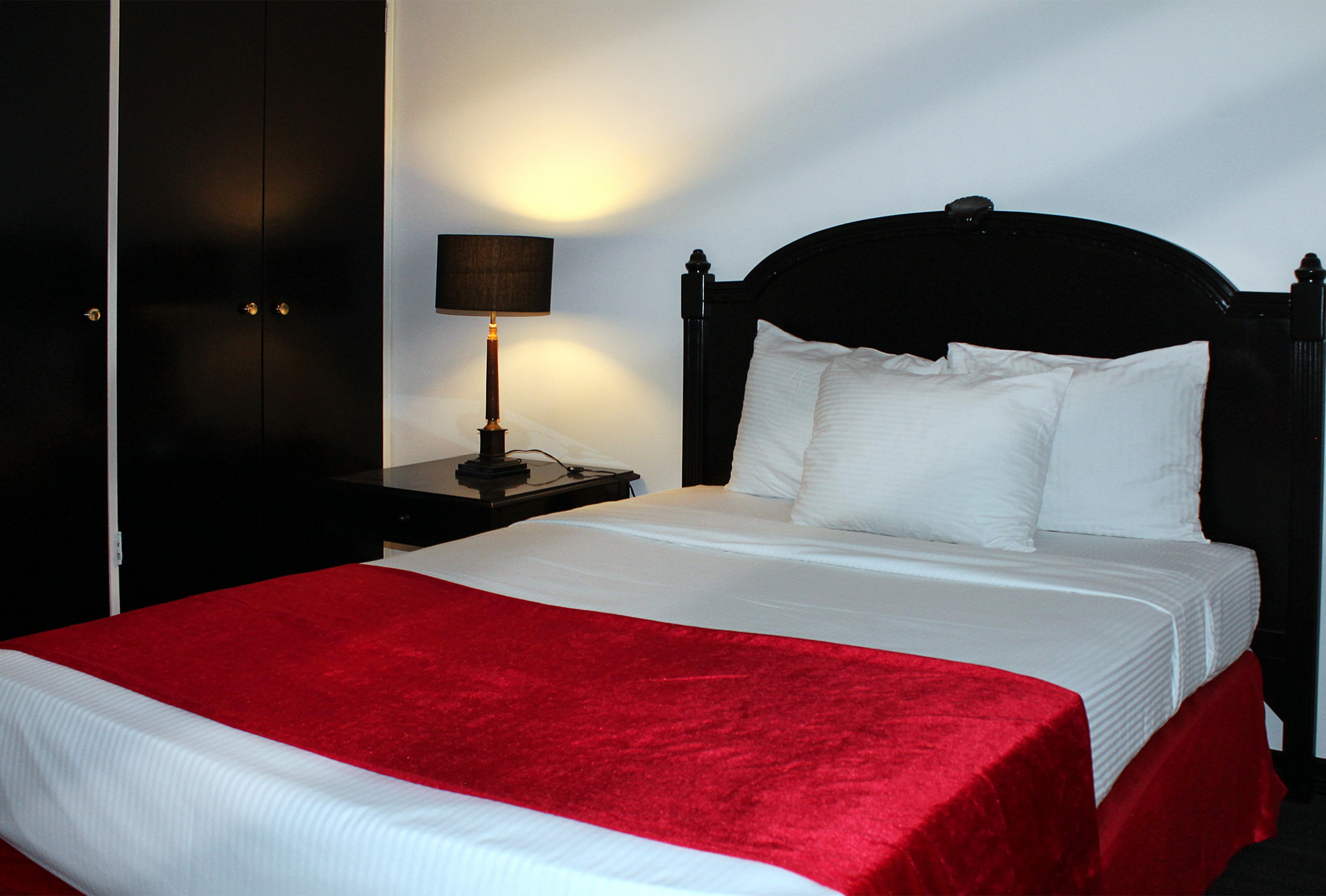 Hotel room with black bed, white linens, red bed runner, and bedside lamp.