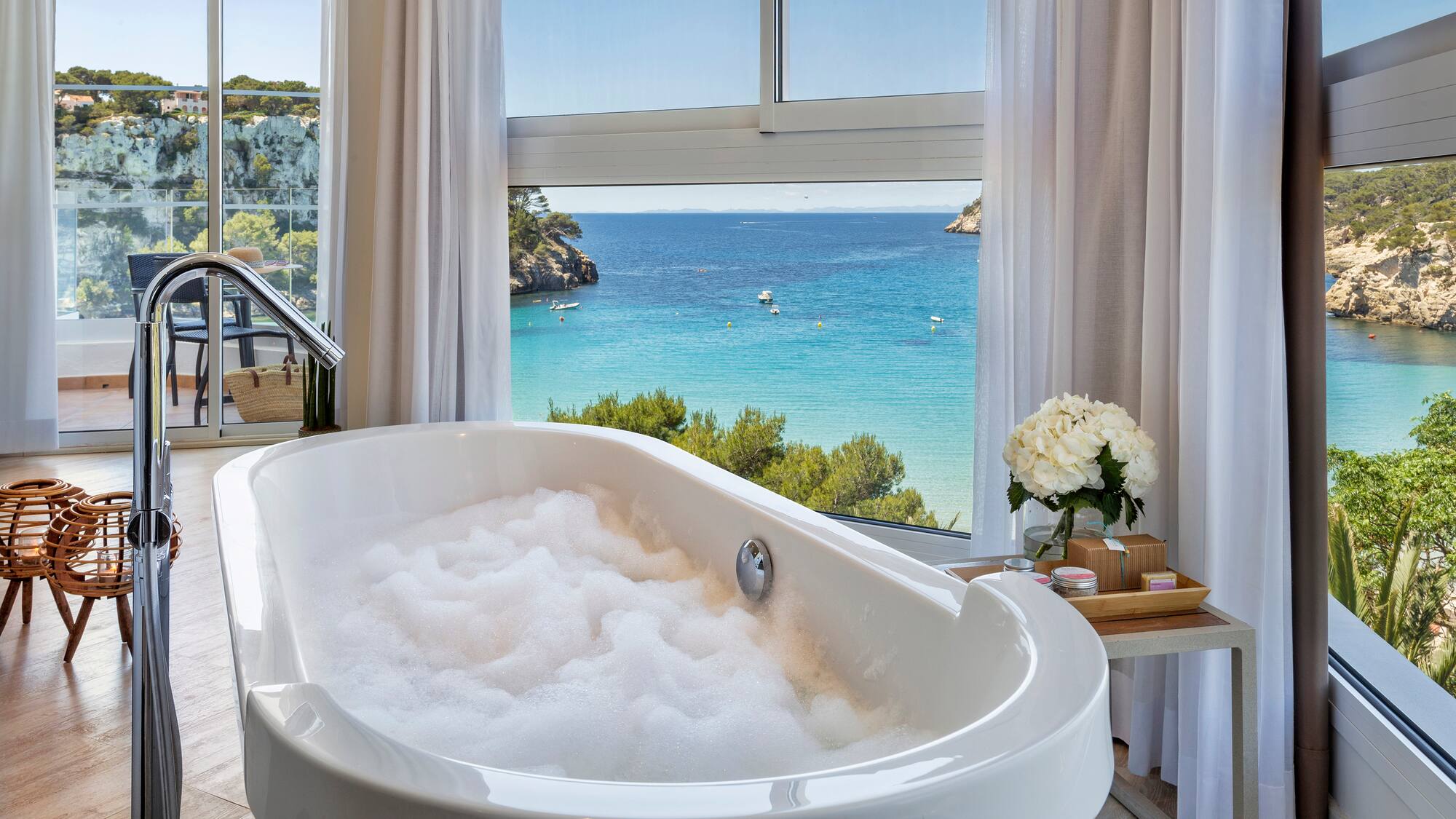 a bathtub with bubbles in front of a window overlooking a body of water