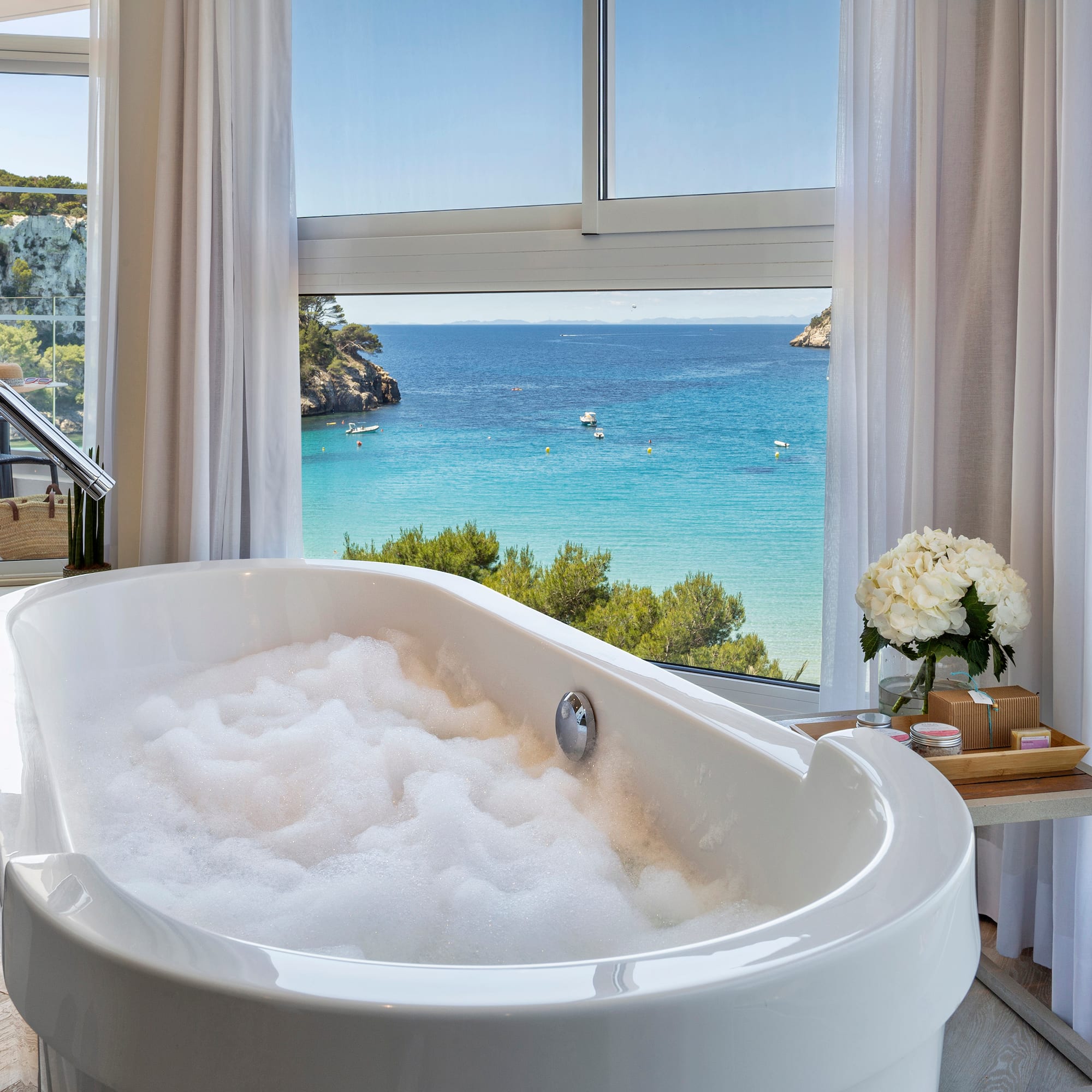 a bathtub with bubbles in front of a window overlooking a body of water