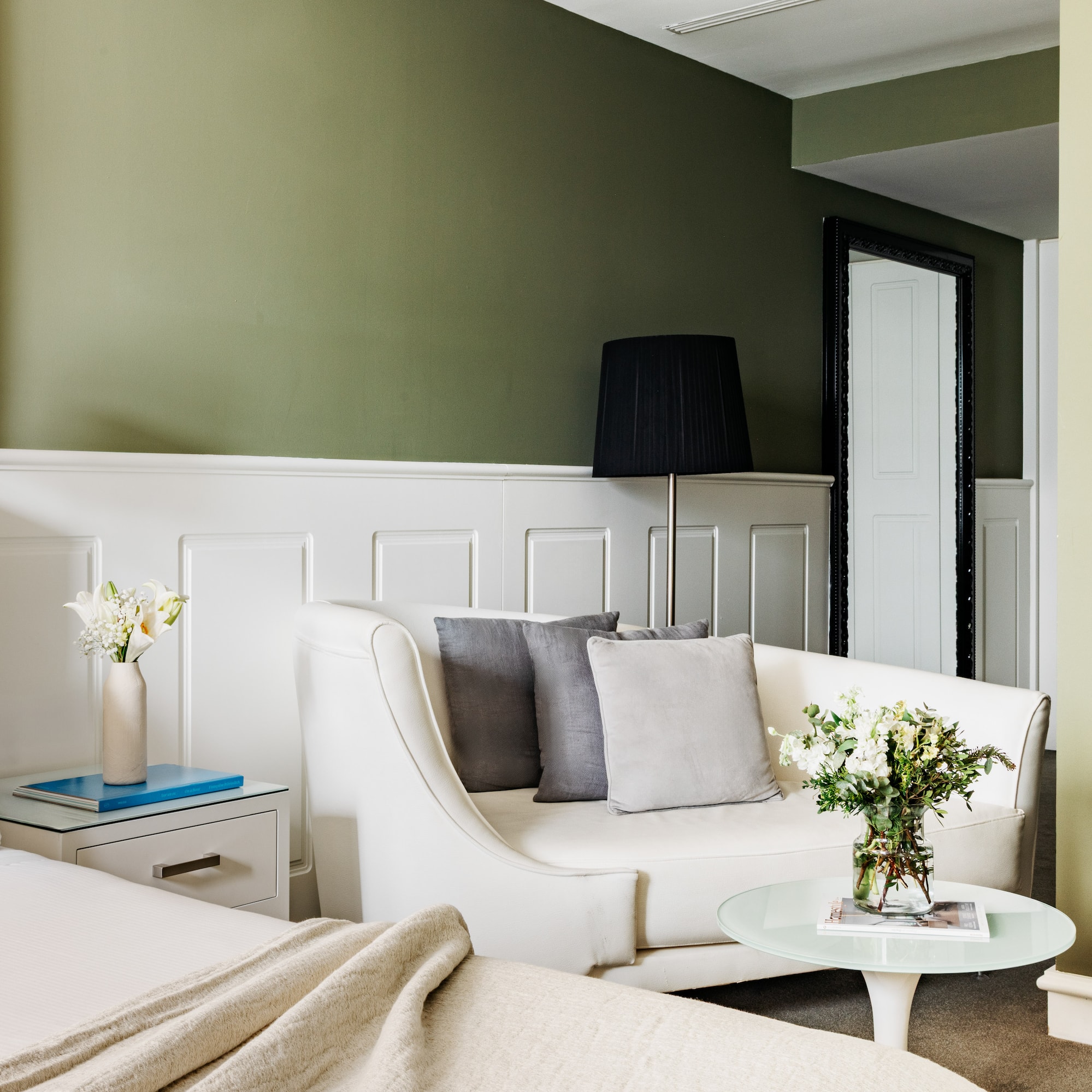 Suite de hotel moderna con cama, sofá y paredes verde oliva, acento dorado.