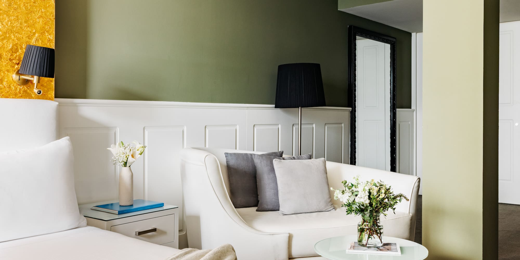 Suite de hotel moderna con cama, sofá y paredes verde oliva, acento dorado.