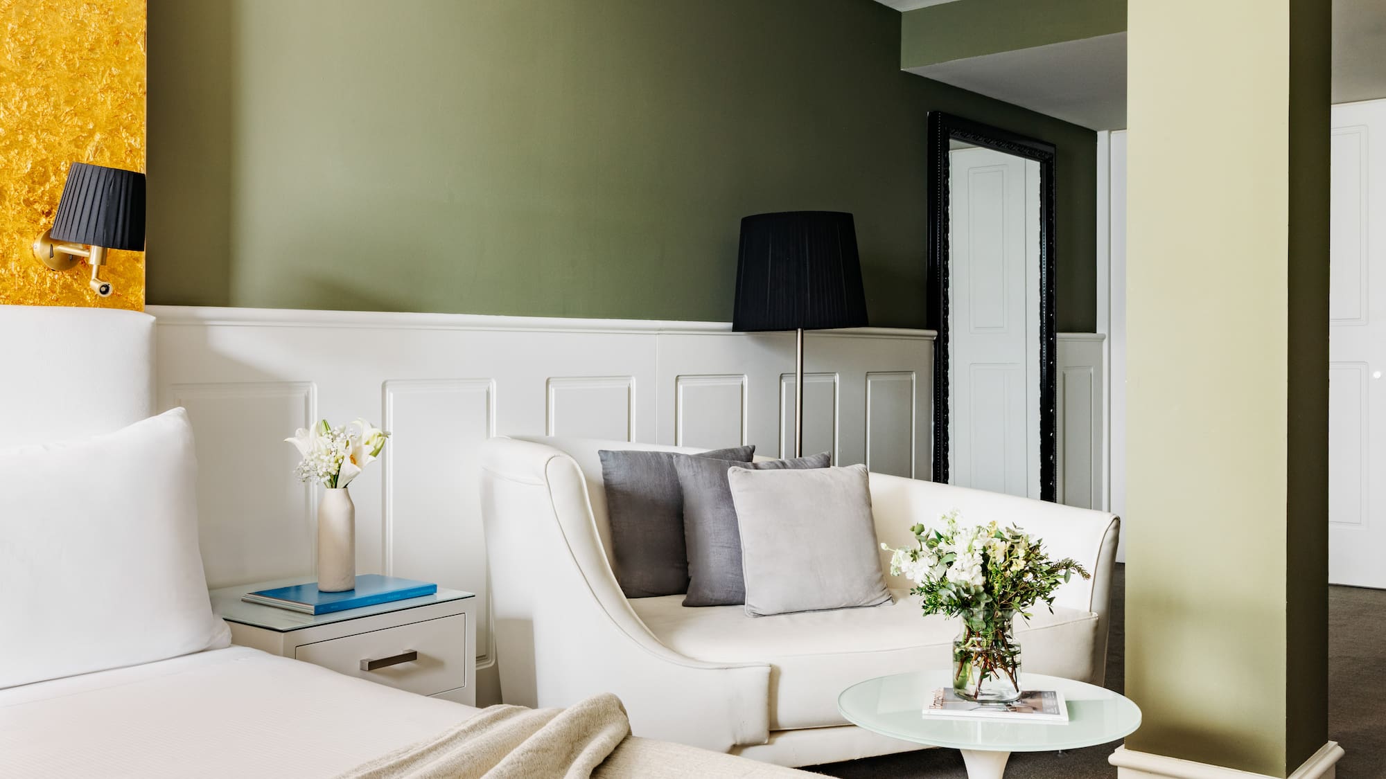 Suite de hotel moderna con cama, sofá y paredes verde oliva, acento dorado.