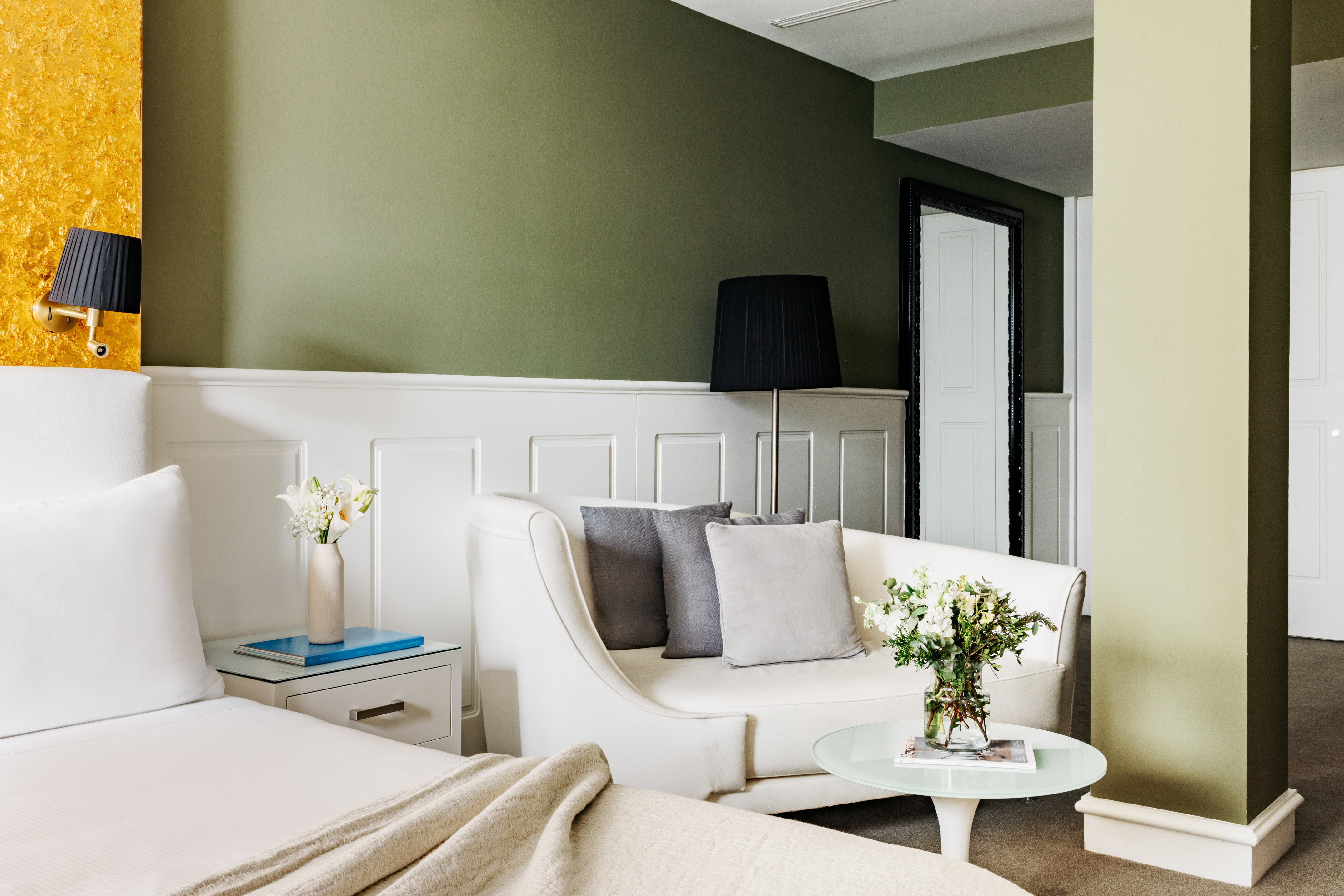 Suite de hotel moderna con cama, sofá y paredes verde oliva, acento dorado.