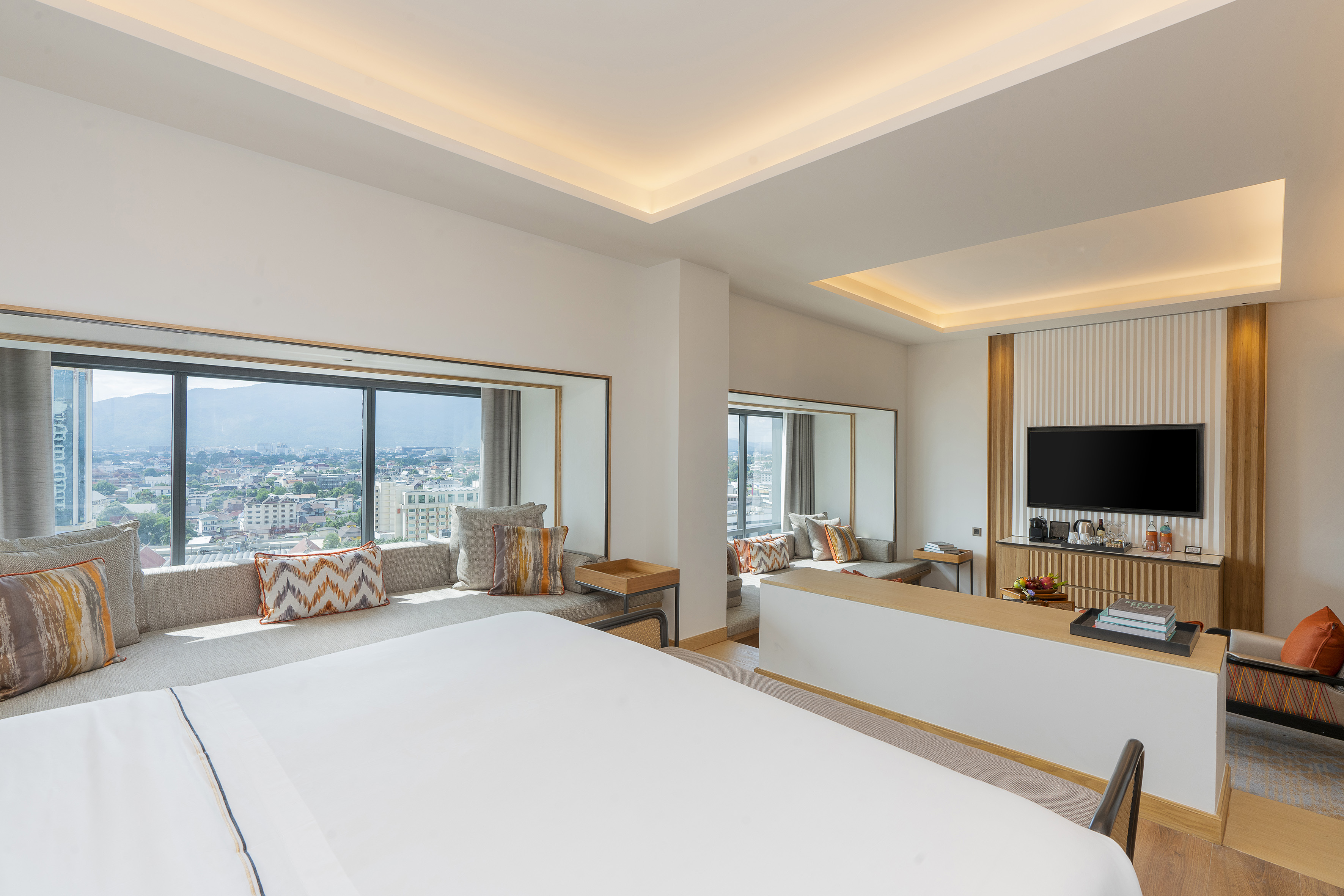 Modern hotel room, city and mountain view, king bed, cozy window seat.