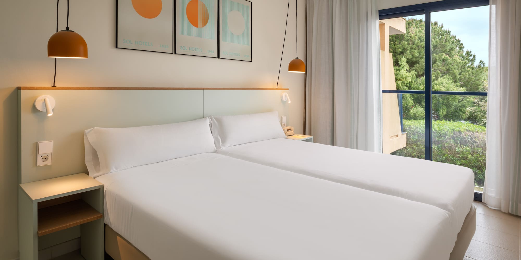 Sol Hotels twin room with modern white beds and window overlooking green trees.