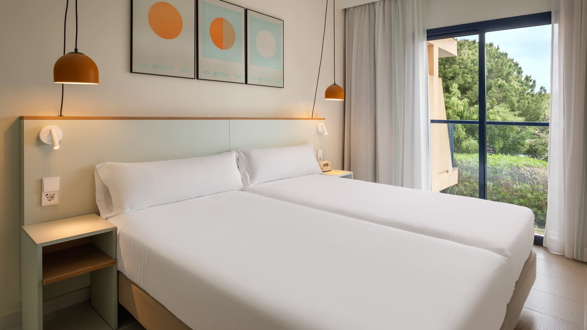 Bright hotel room with twin beds, white sheets, and a window to lush nature.