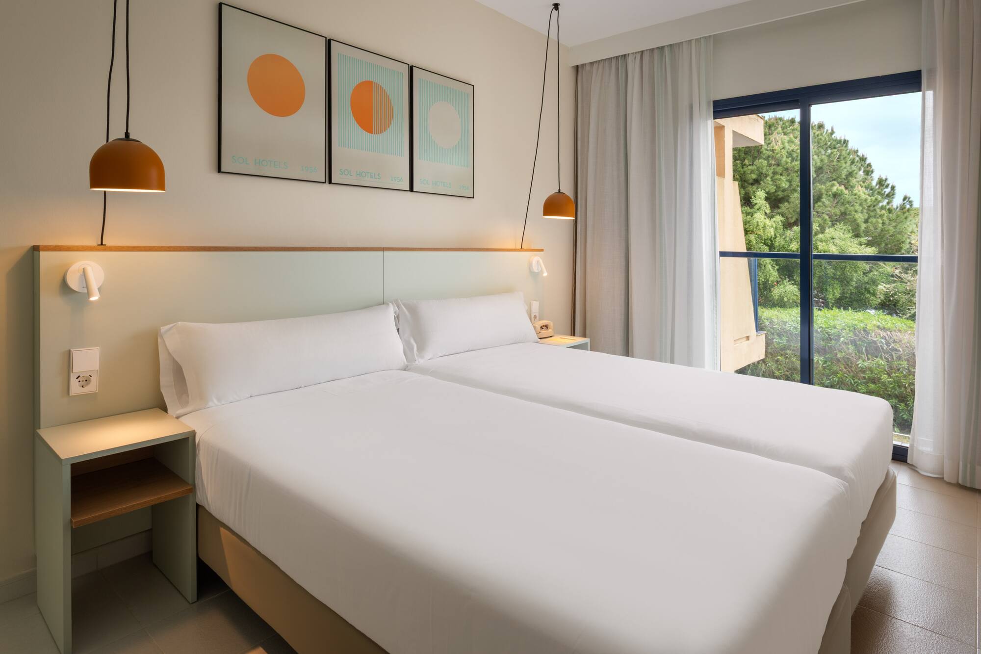 Sol Hotels twin room with modern white beds and window overlooking green trees.