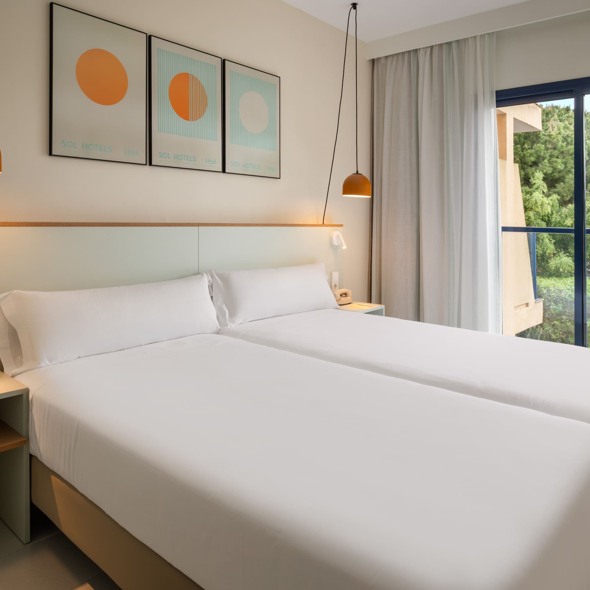 Sol Hotels twin room with modern white beds and window overlooking green trees.
