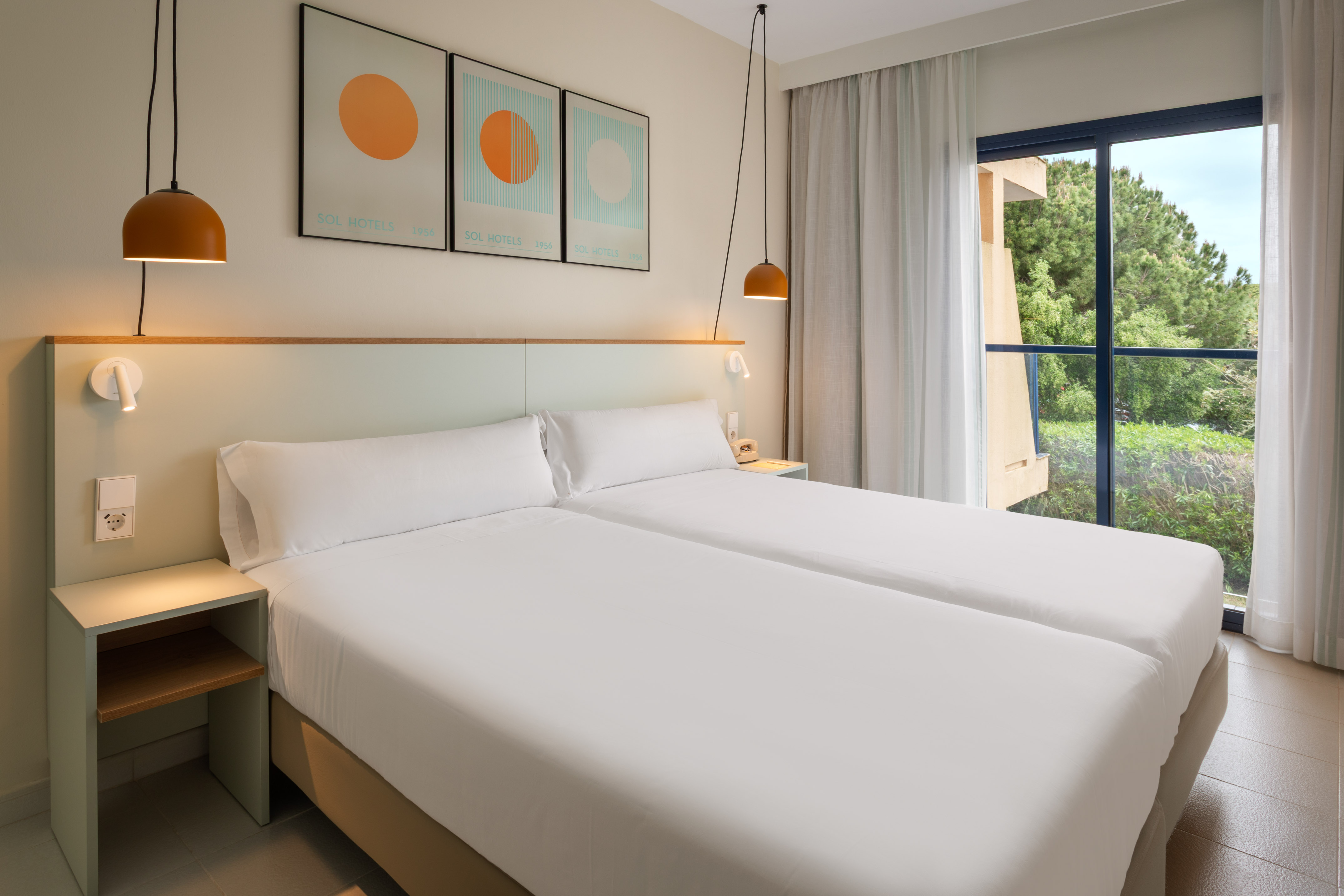 Bright hotel room with twin beds, white sheets, and a window to lush nature.