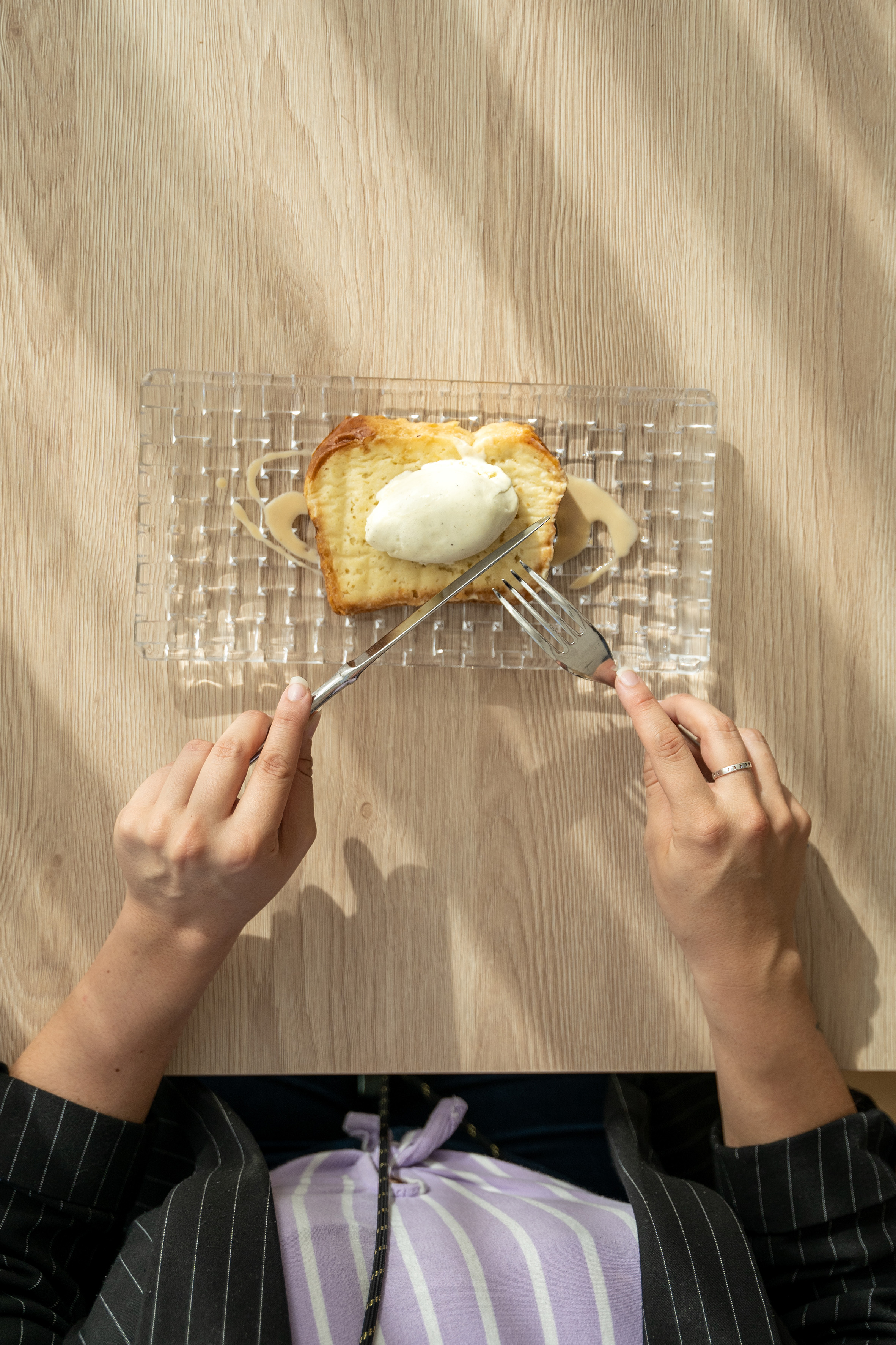 Hands cutting brioche cake with ice cream and caramel sauce on wood.