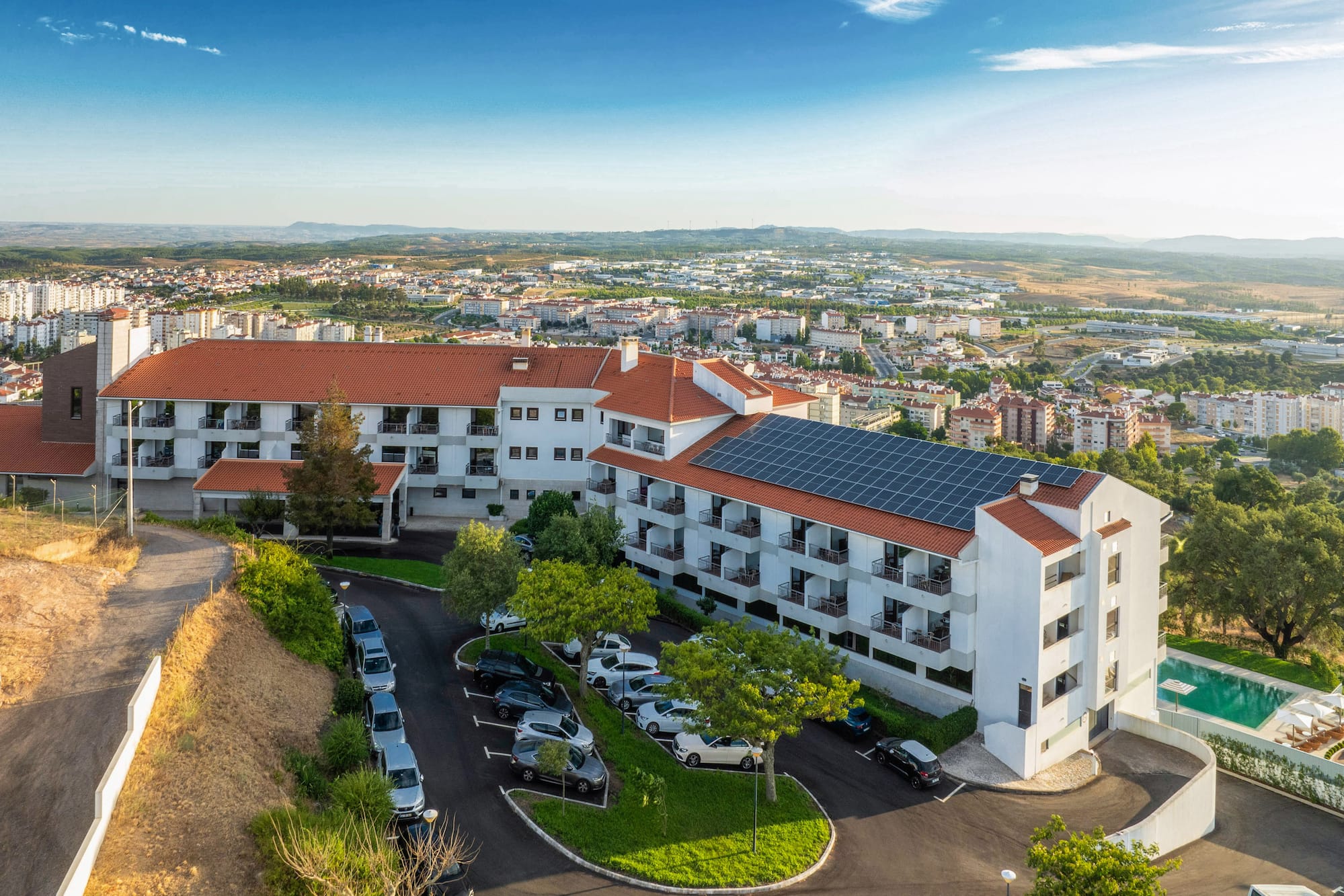 Sustainable hotel with solar panels, parking, and pool overlooking a city.