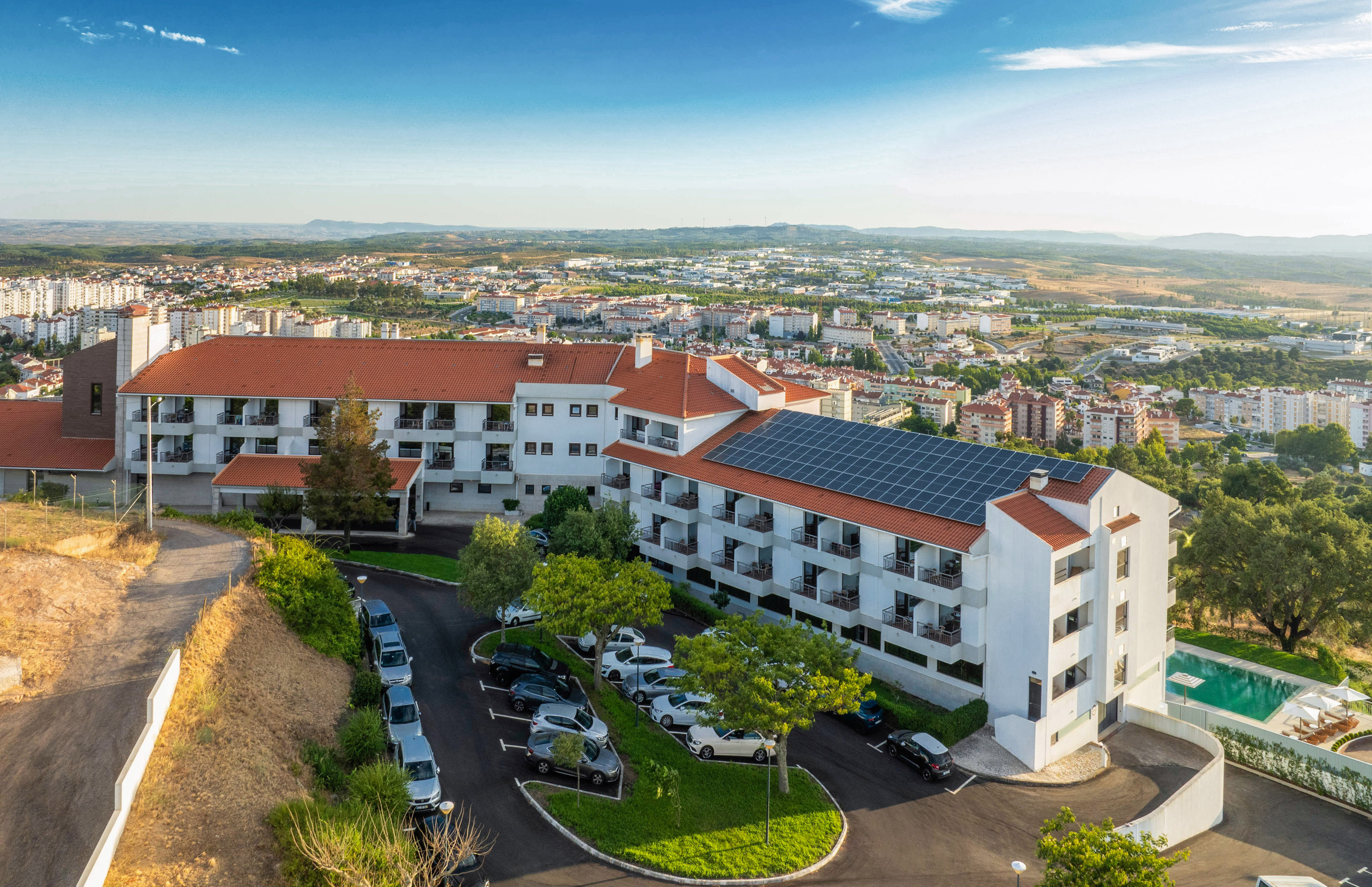 Sustainable hotel with solar panels, parking, and pool overlooking a city.