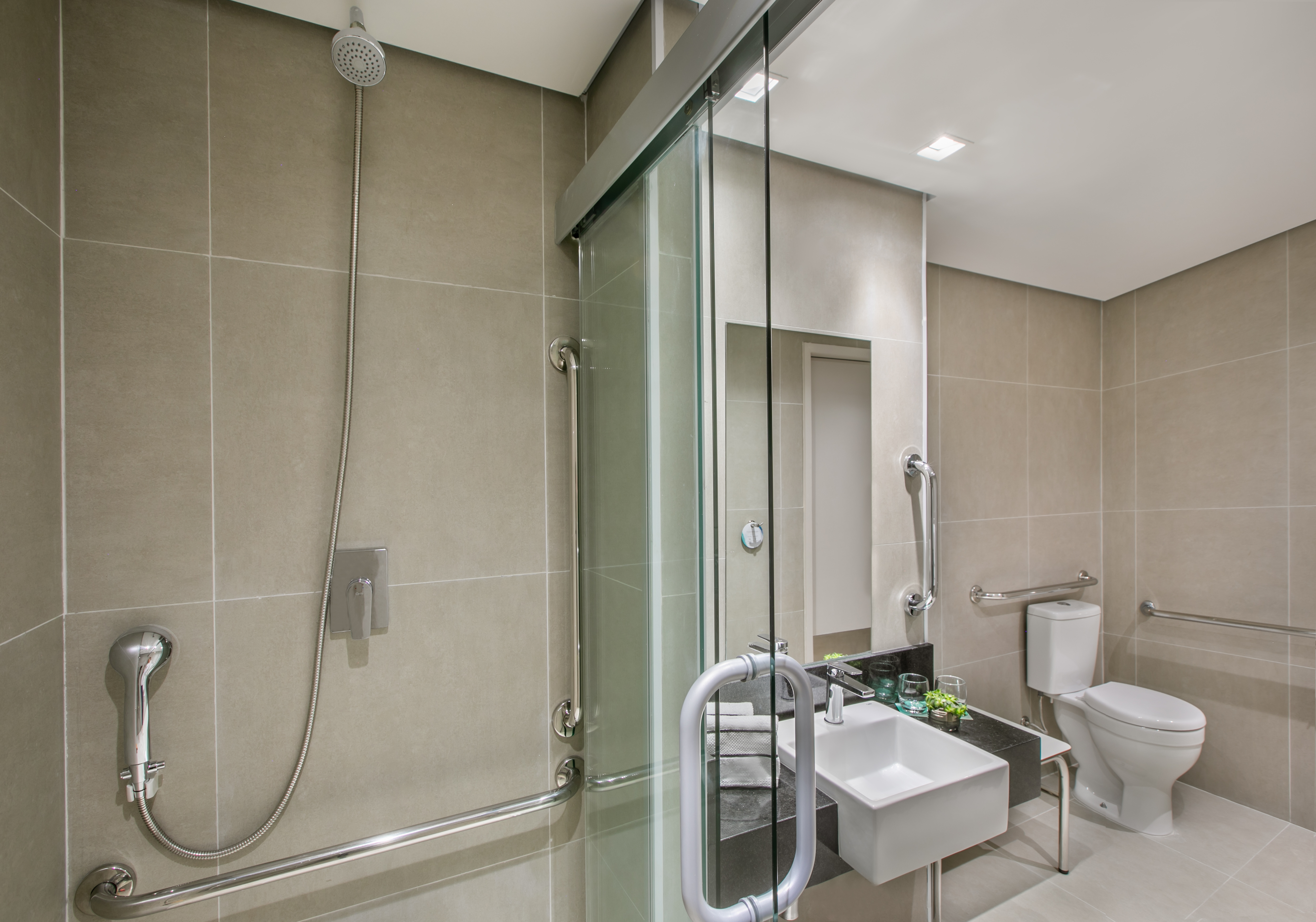 Accessible modern bathroom with glass shower, grab bars, sink, and toilet.