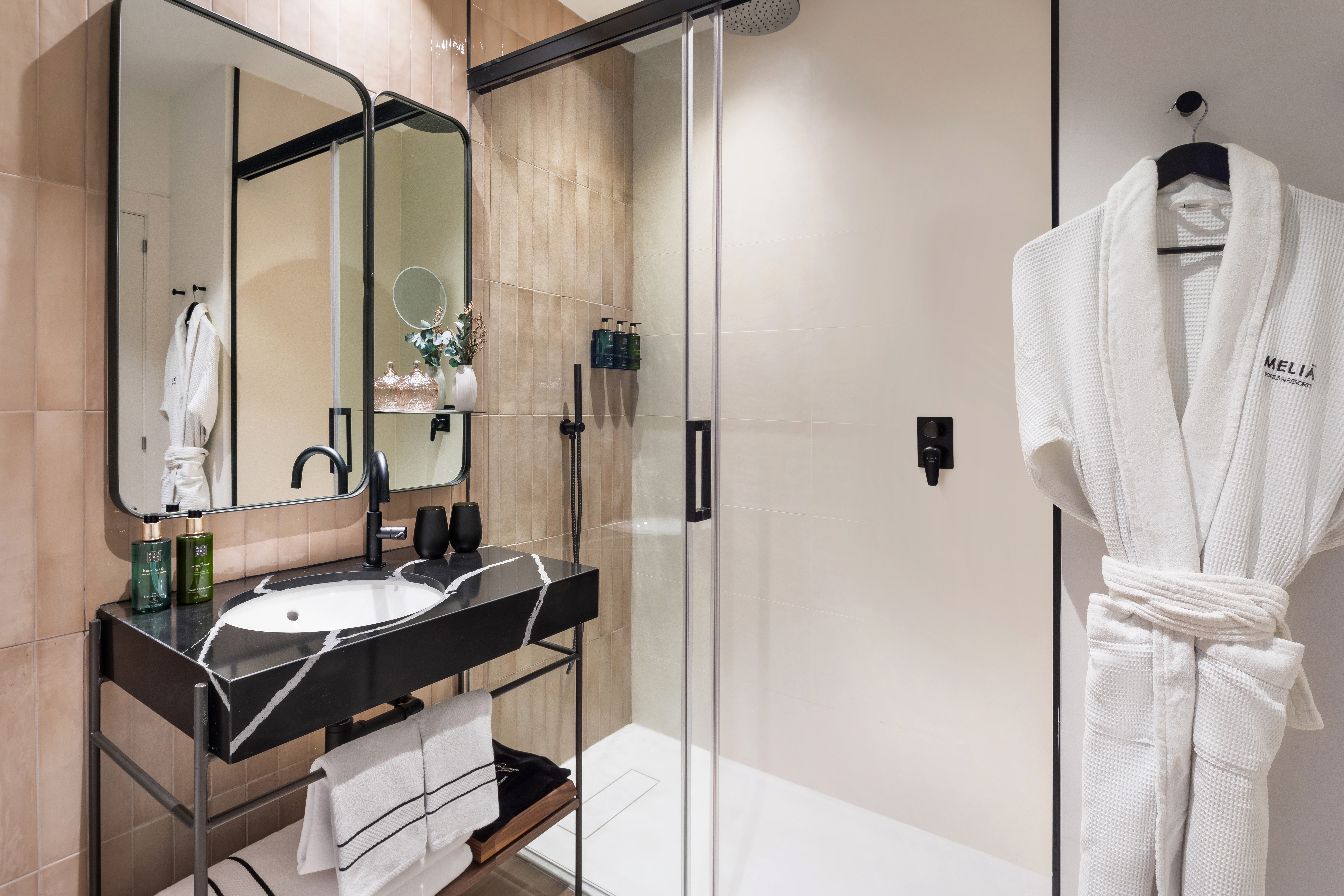 Modern hotel bathroom with black marble vanity, walk-in shower, and Melia bathrobe.
