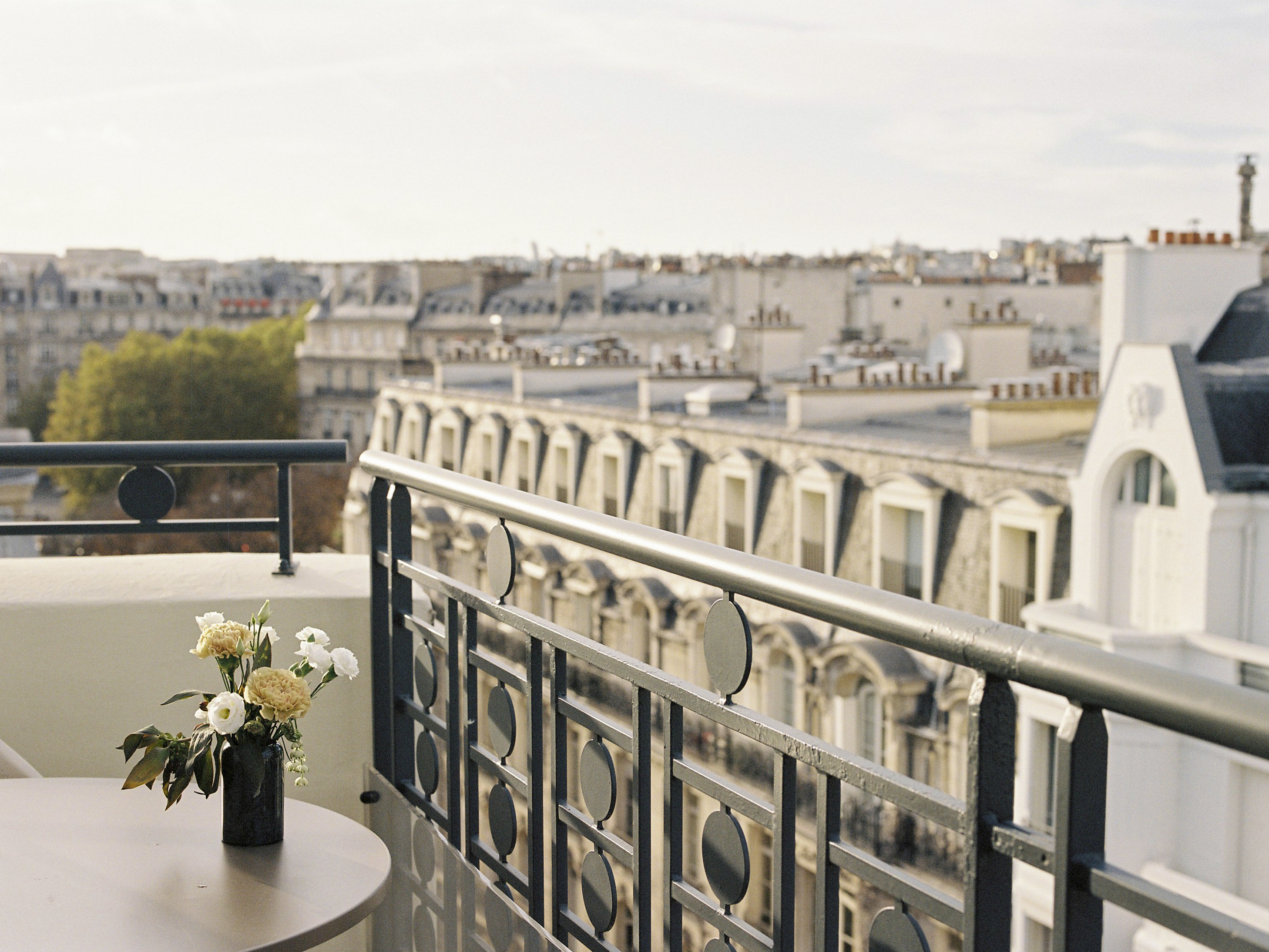 Paris balcony, flowers on table, panoramic view of city rooftops.