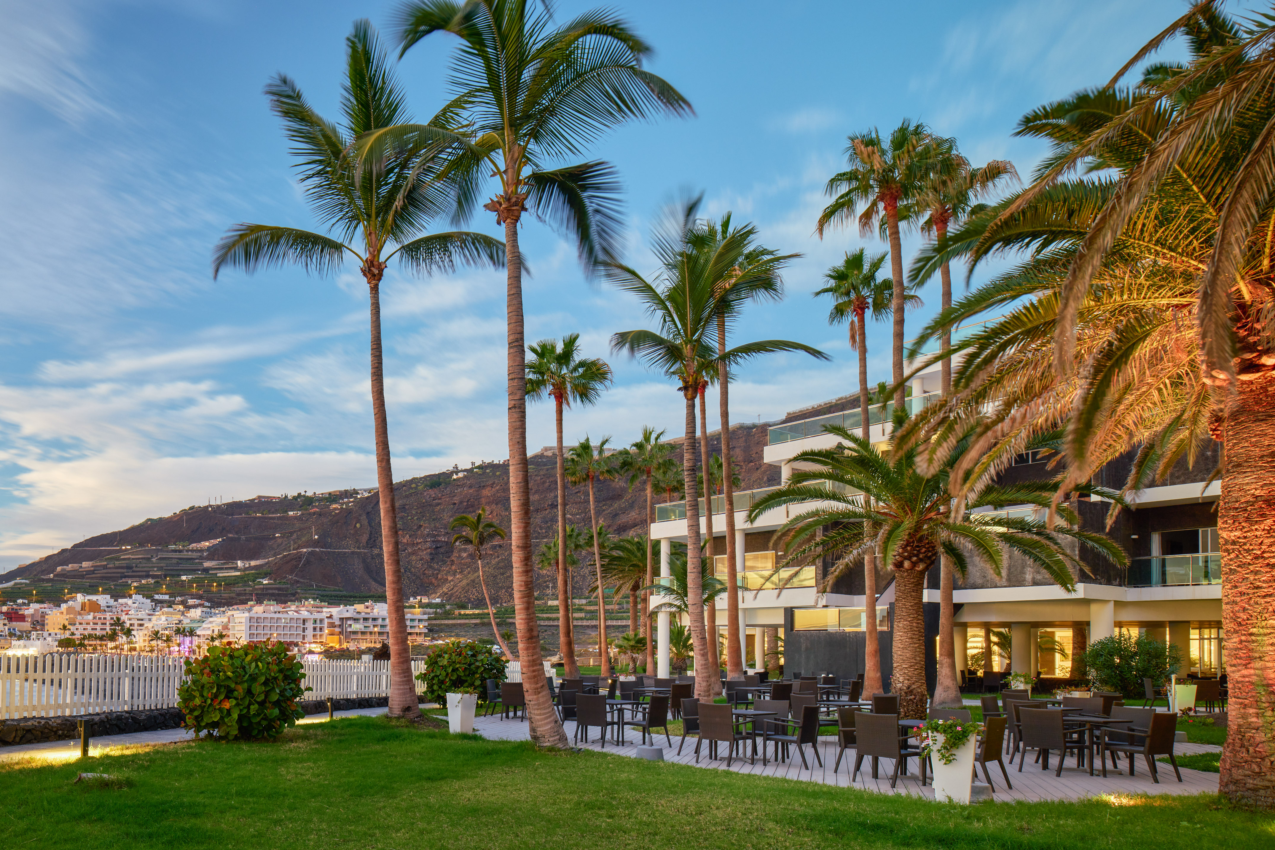 Resort outdoor dining terrace with palm trees and mountain backdrop.