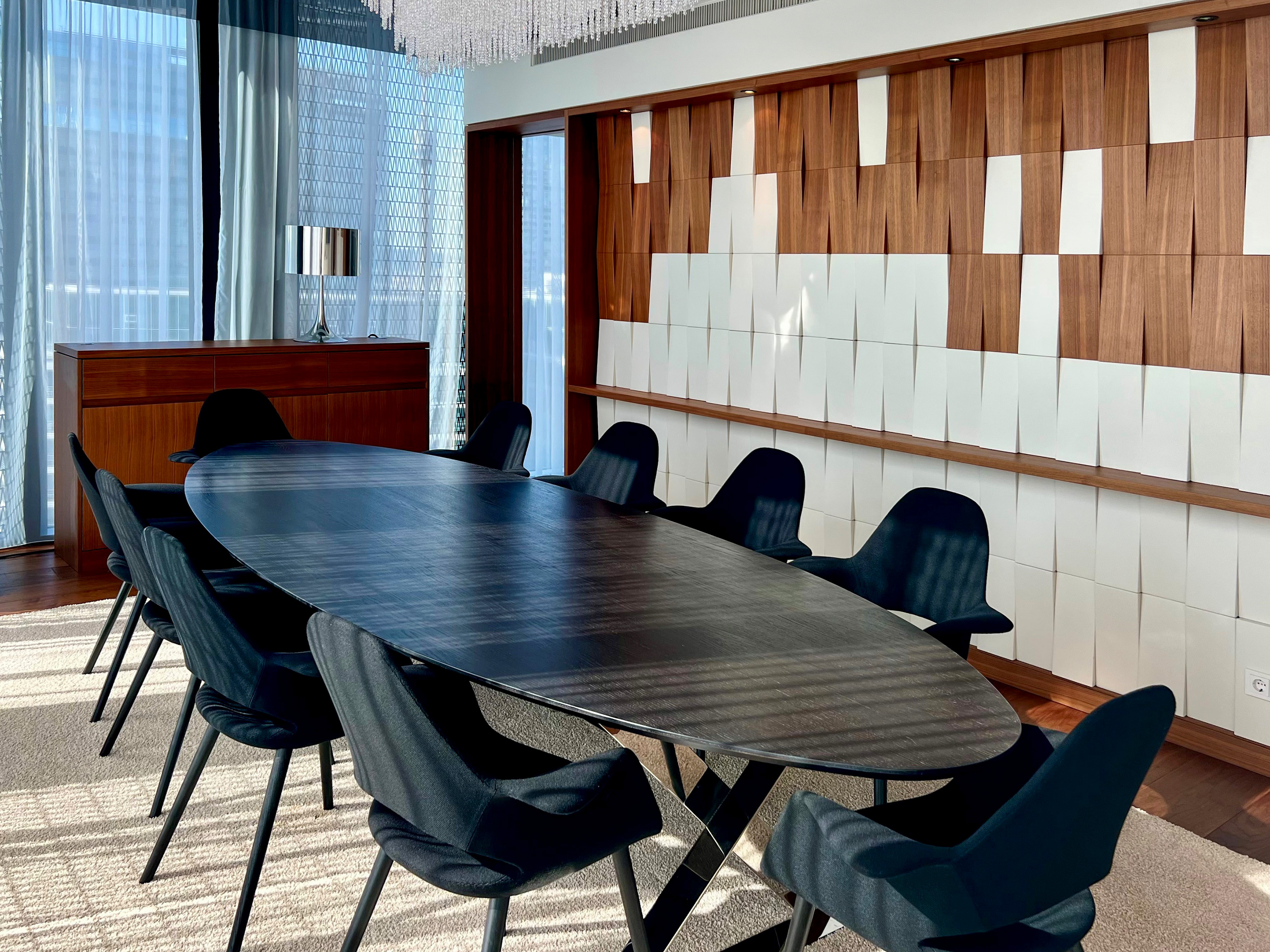 Modern dining room with large oval table, black chairs, and textured wood/white wall.