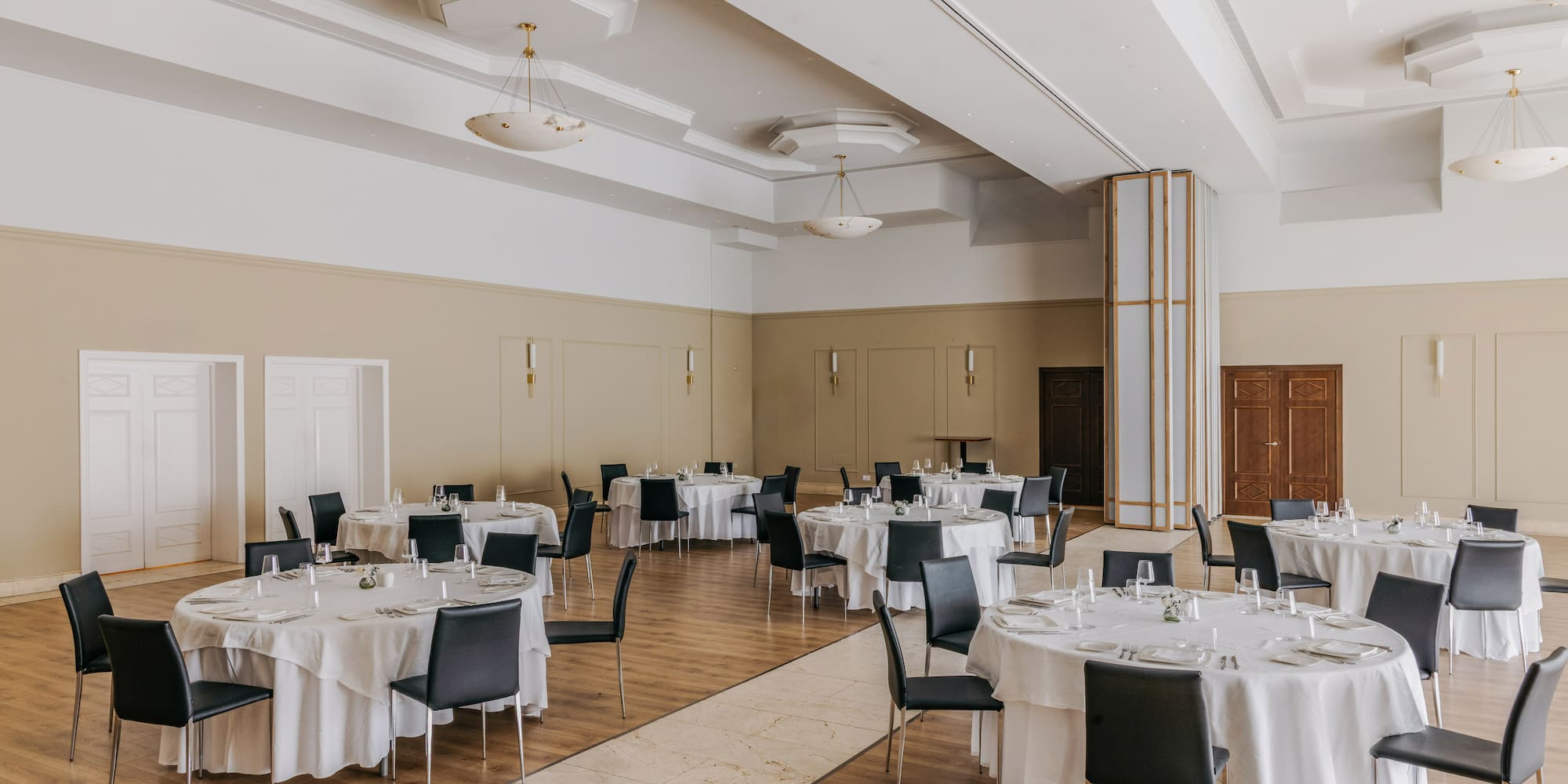 Elegant banquet hall set with round dining tables, white tablecloths, and black chairs.
