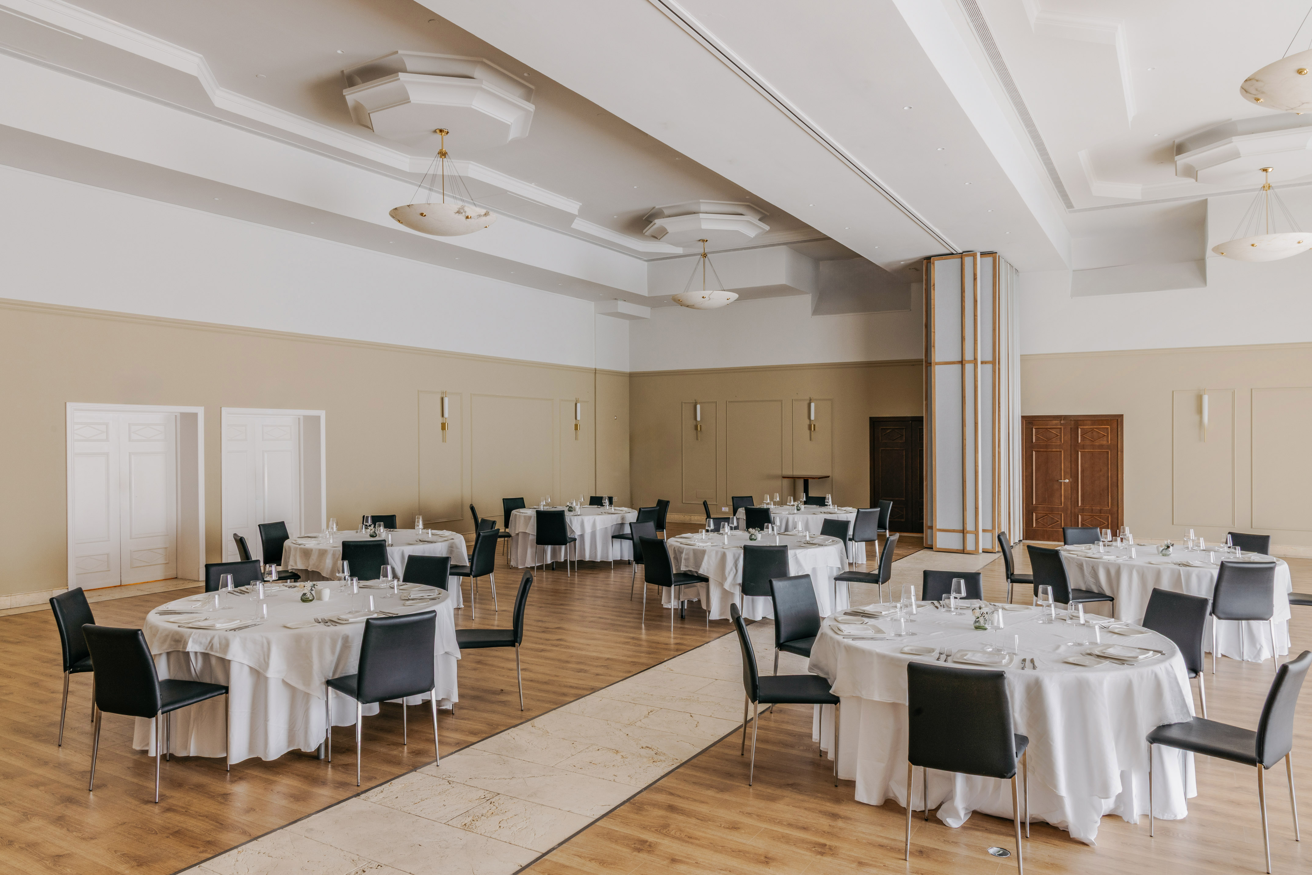 Elegant banquet hall with set round tables, white tablecloths, and black chairs.