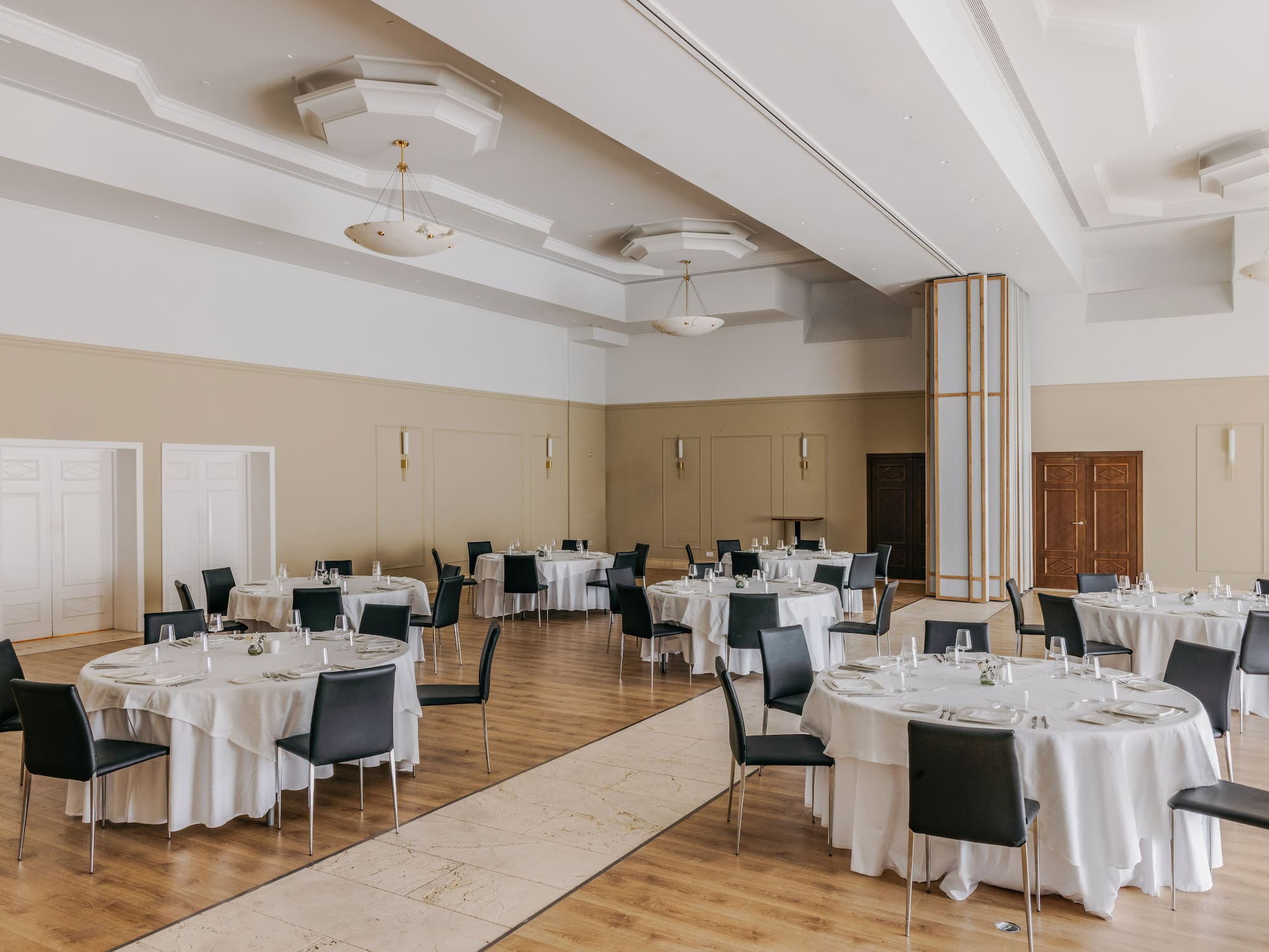 Elegant banquet hall with set round tables, white tablecloths, and black chairs.