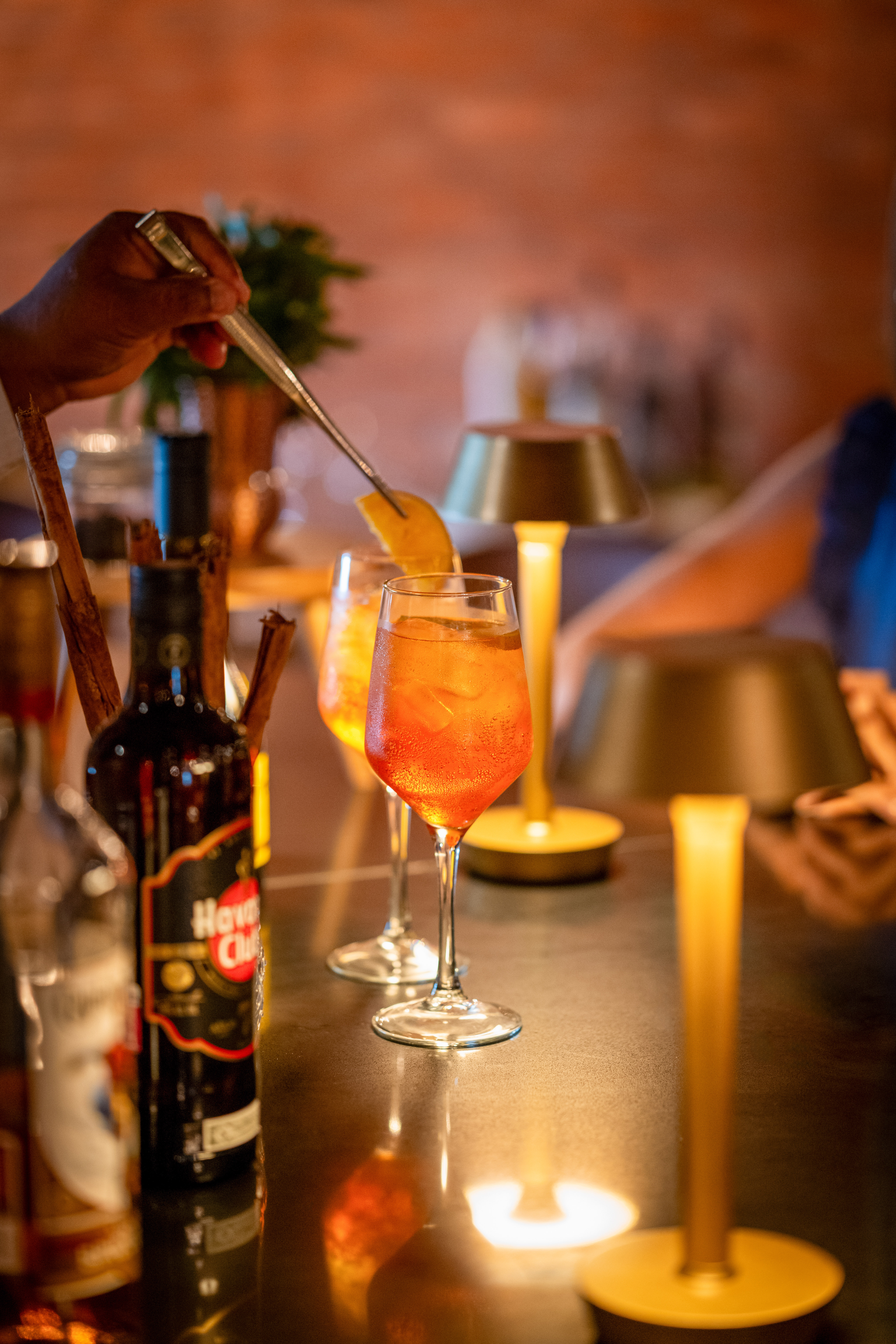 Bartender garnishing an orange Aperol Spritz with an orange slice at a bar.