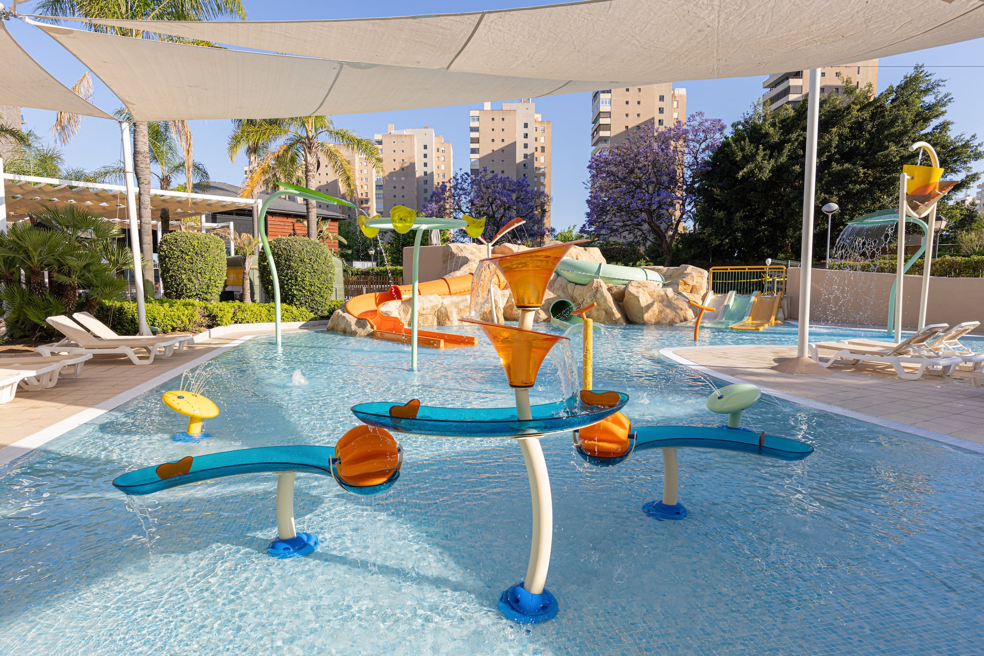 Kids' water park with colorful slides, splash features, palm trees, and resort buildings.