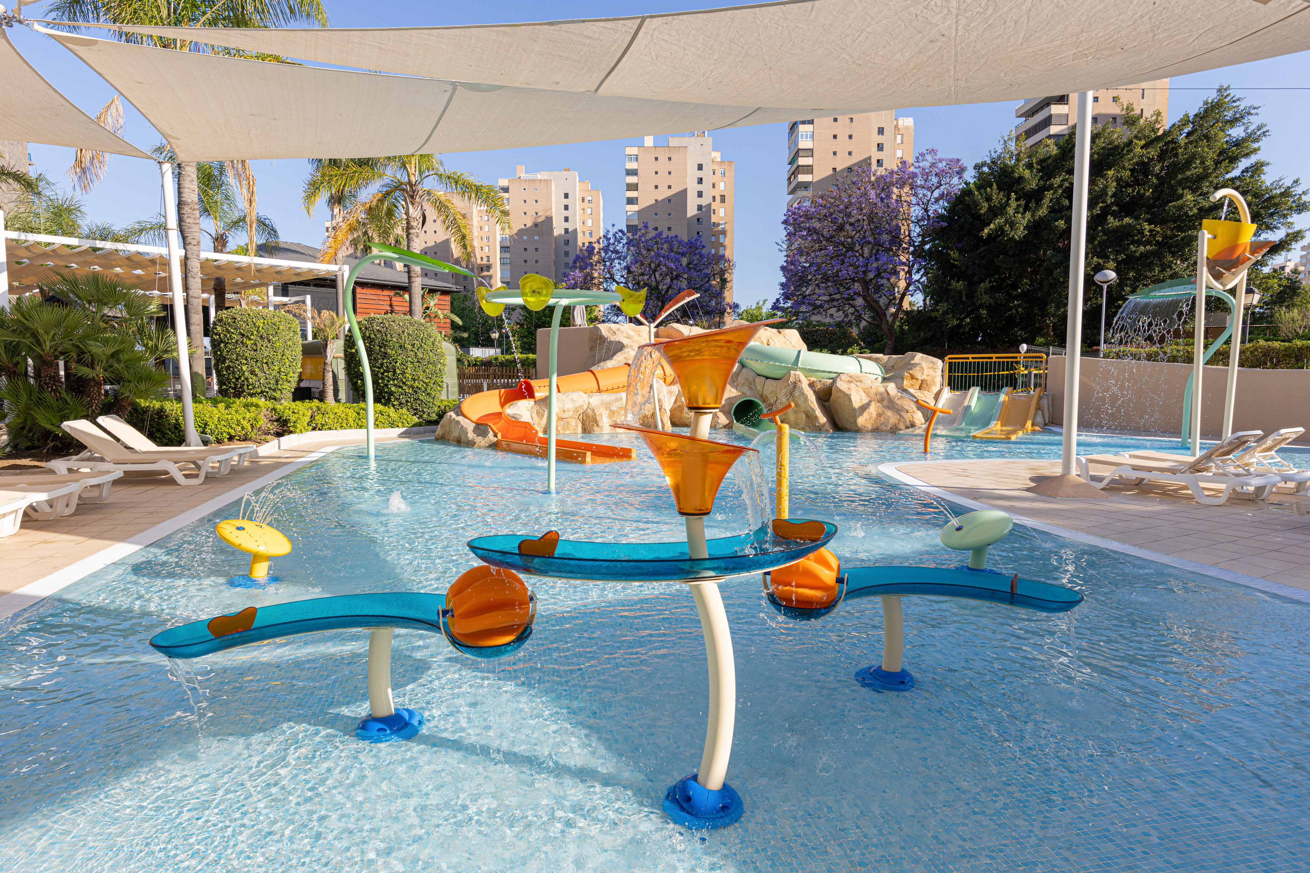 Kids' water park with colorful slides, splash features, palm trees, and resort buildings.