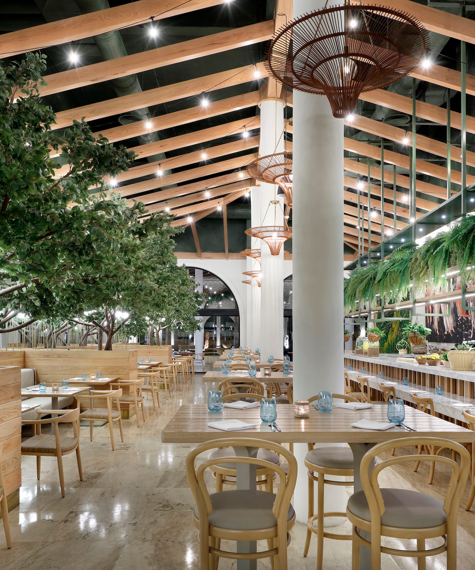 Modern restaurant with indoor trees, wood ceilings, dining tables, and bar.
