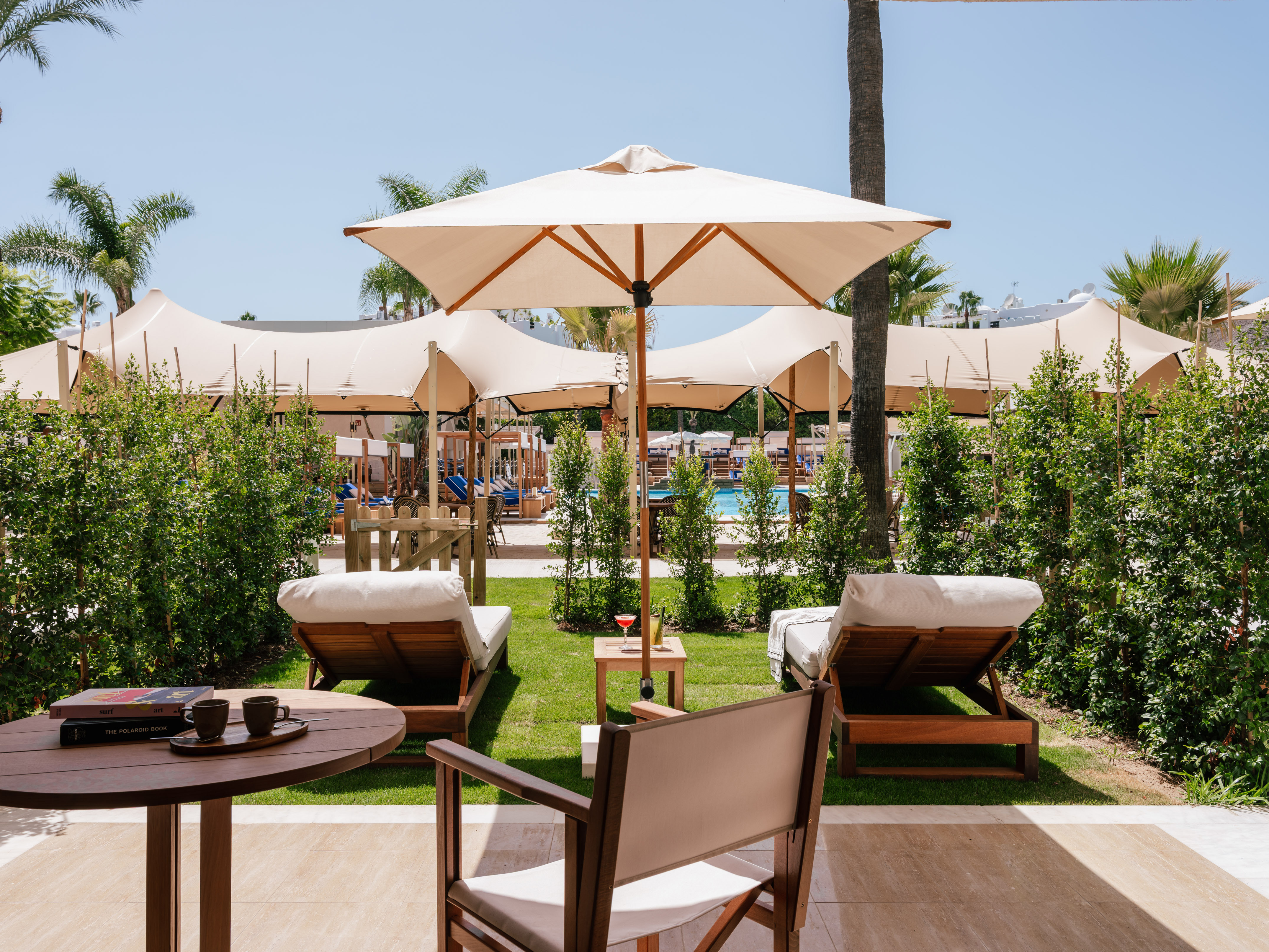 Luxury resort pool lounge with sun loungers, beige parasols, and lush greenery.