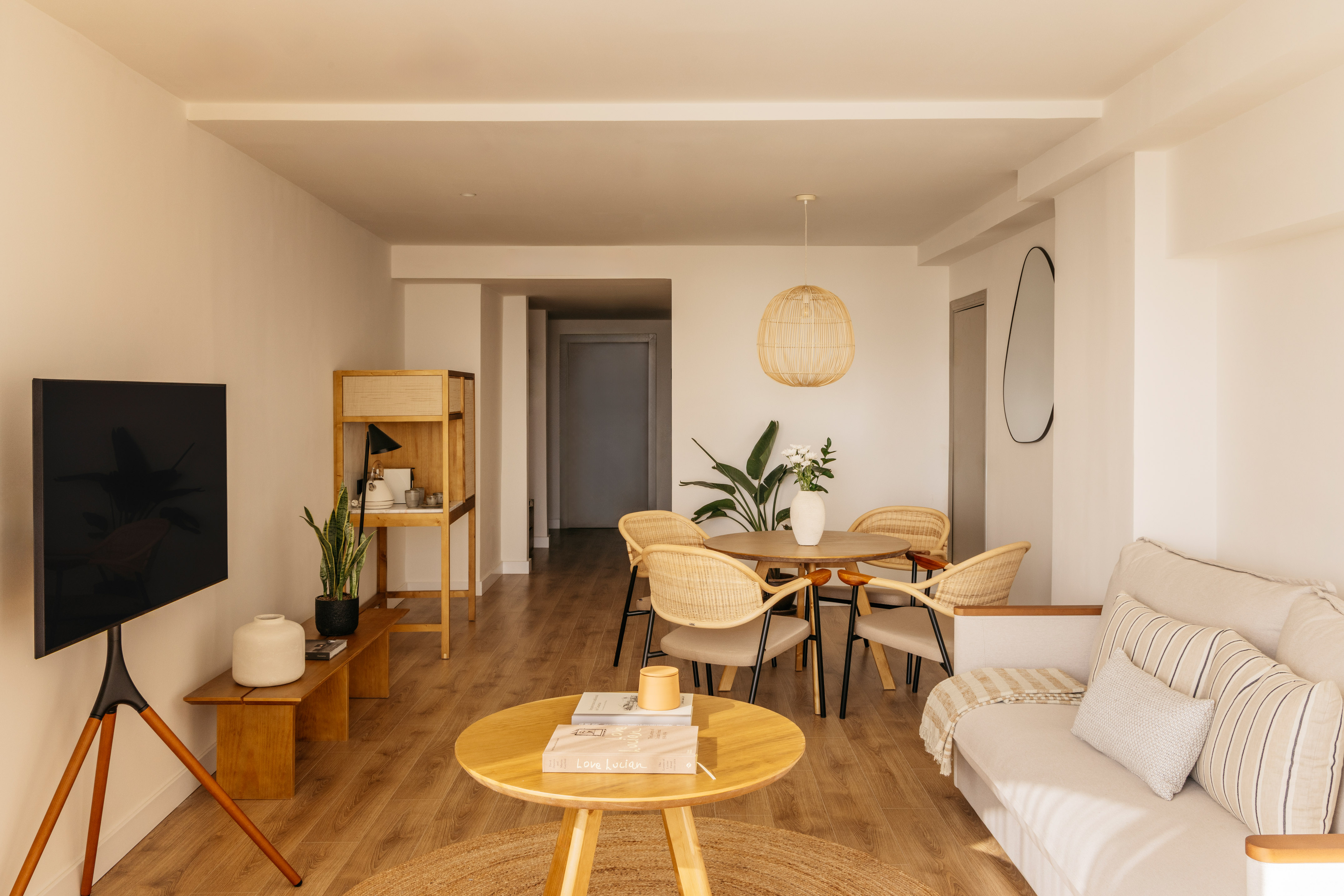 Bright modern living-dining room with rattan chairs, wooden furniture, and plants.