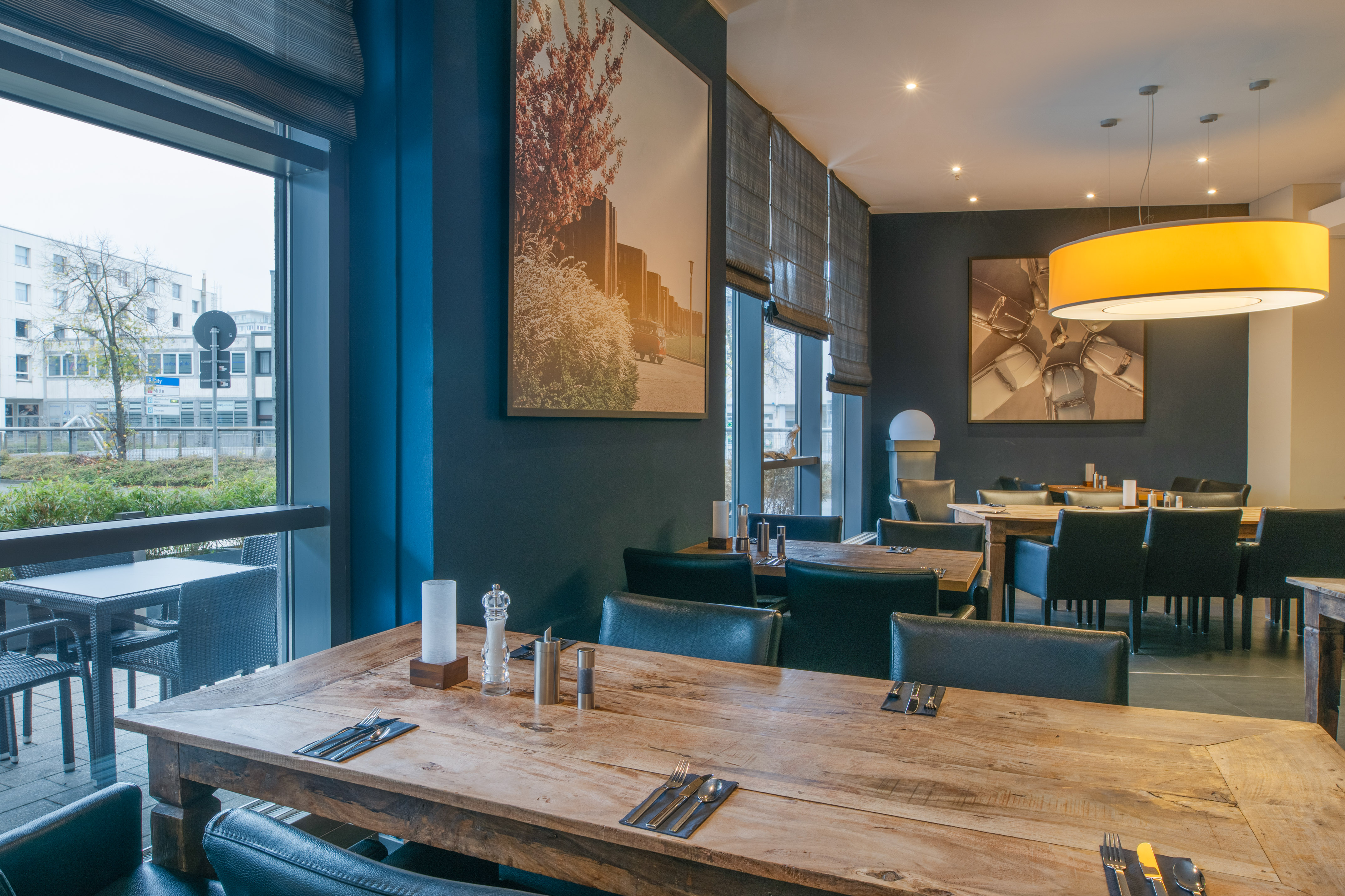Modern restaurant interior with wooden tables, dark chairs, and large windows.