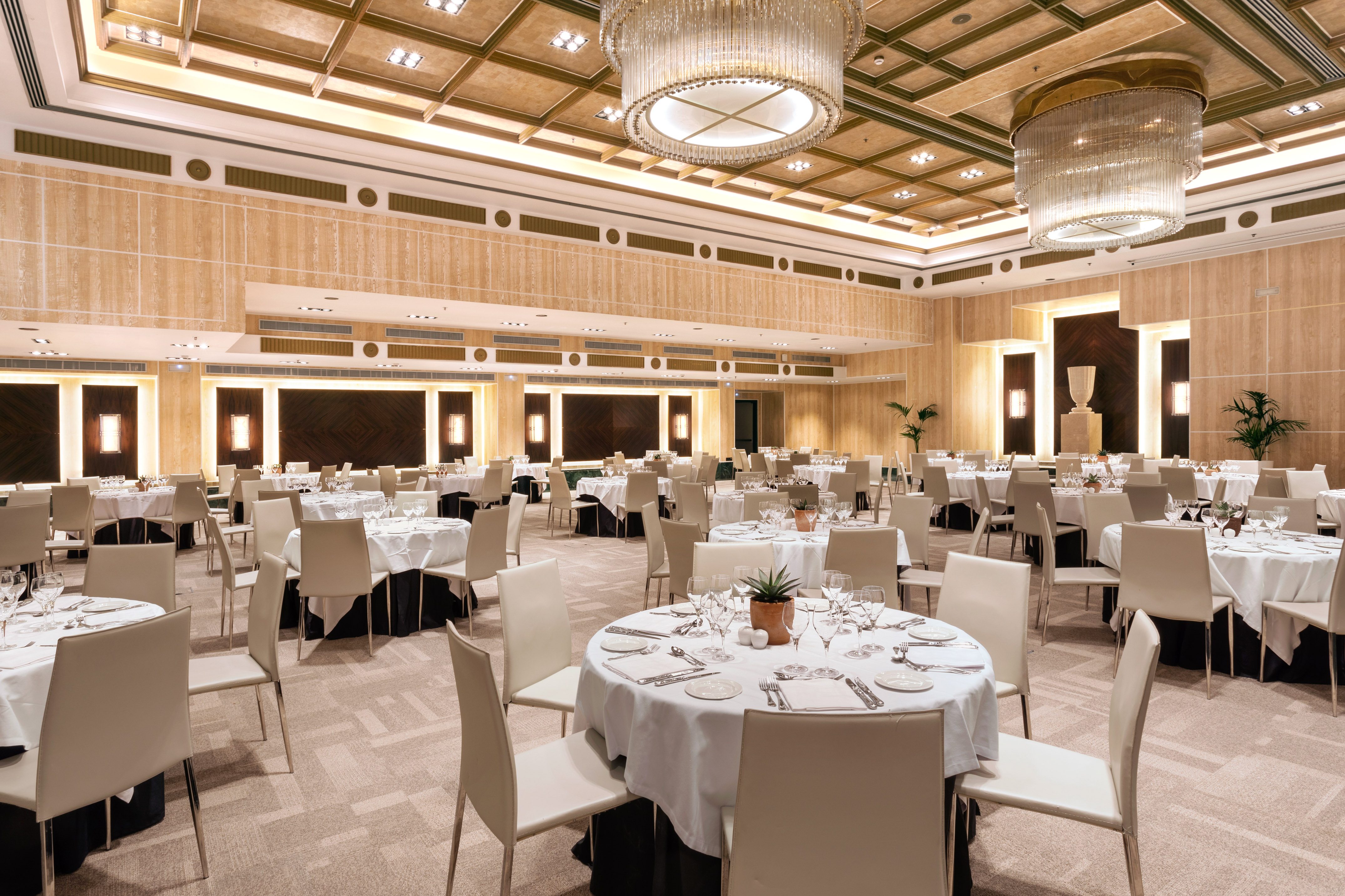 Elegant hotel ballroom with round dining tables and chandeliers.