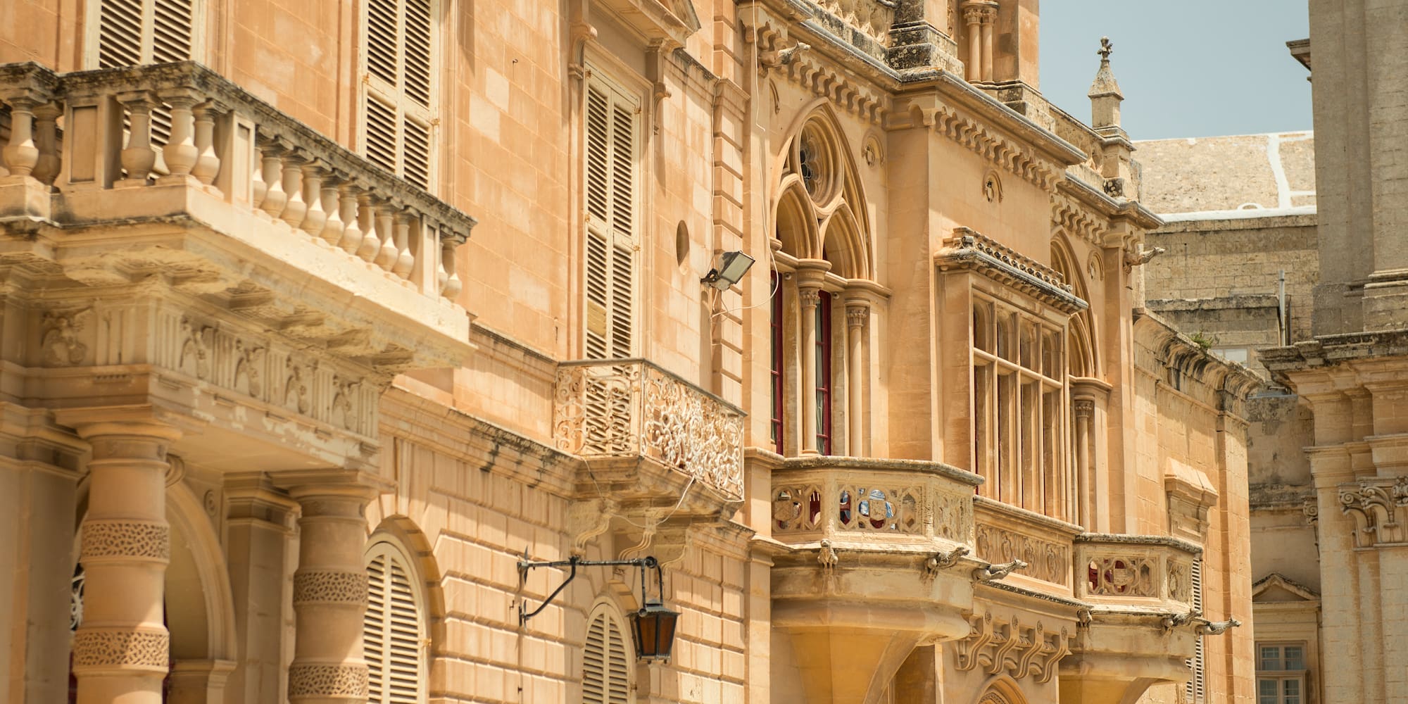 Ornate Baroque limestone palace in Mdina, Malta, with balconies and shutters.