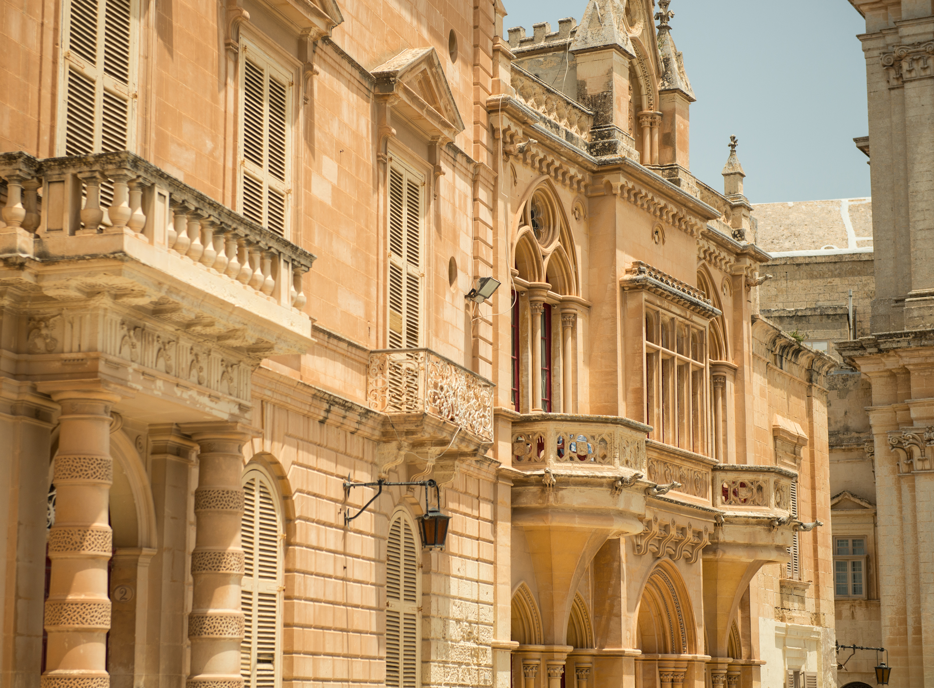 Ornate Baroque limestone palace in Mdina, Malta, with balconies and shutters.